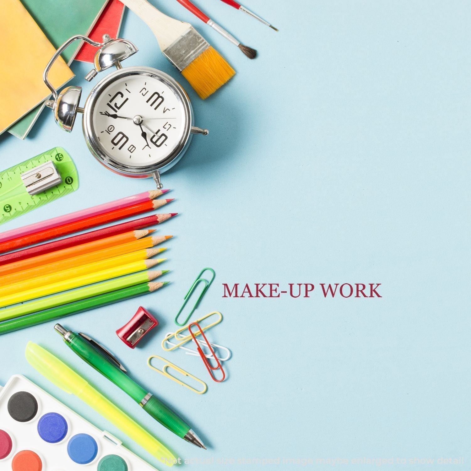 Self Inking Make Up Work Stamp on a blue desk with colorful pencils, paintbrushes, paper clips, an alarm clock, and a ruler.