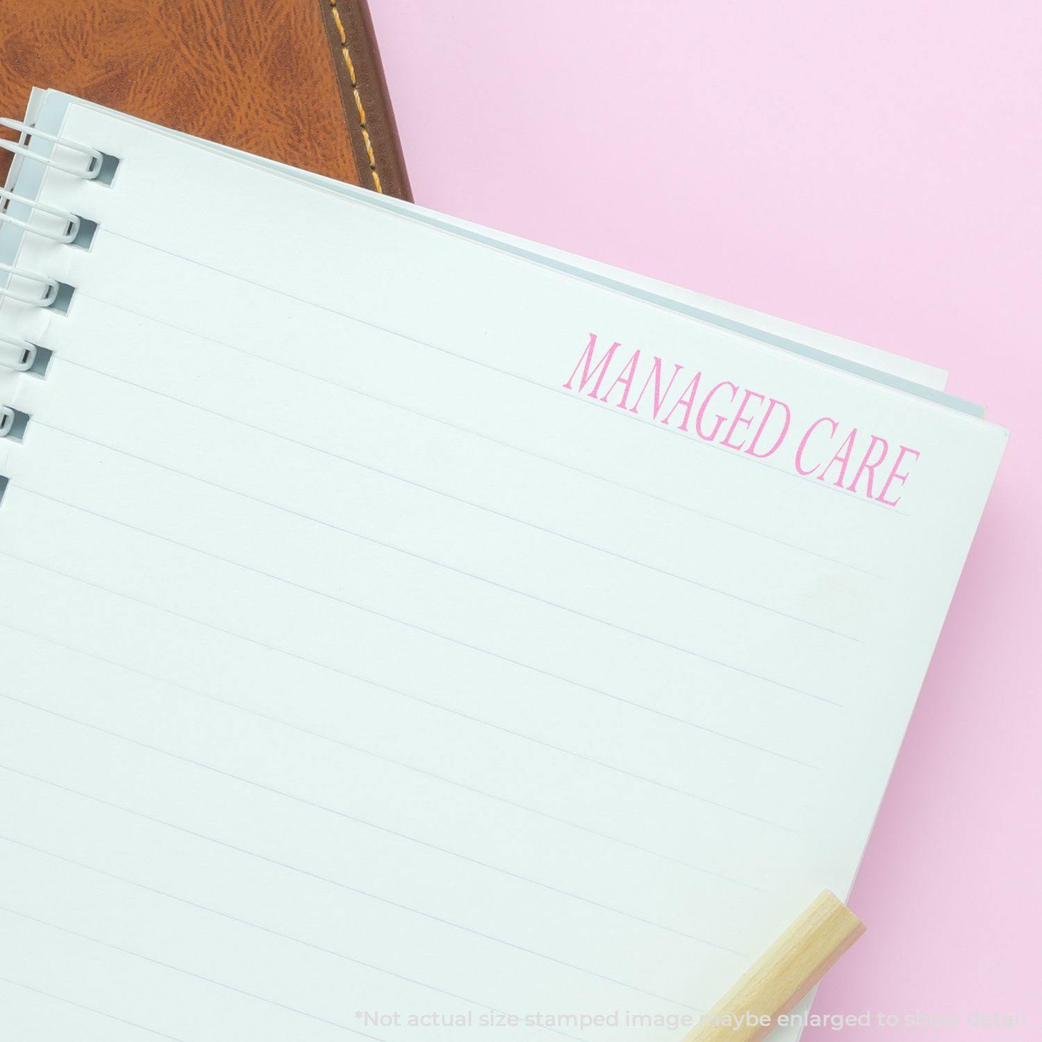 A notebook with a Managed Care rubber stamp imprint in pink on the top right corner, placed on a pink surface.