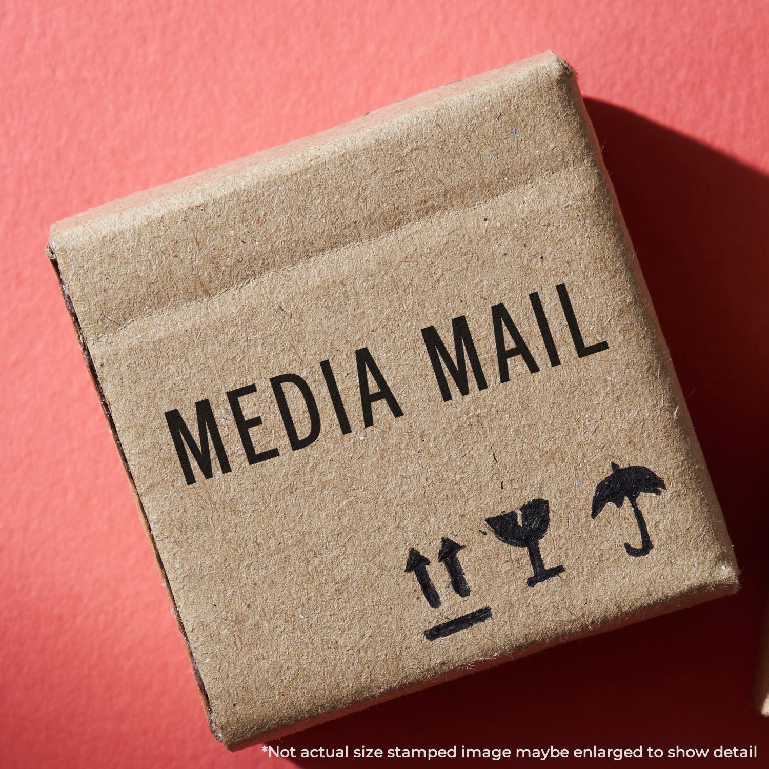 A cardboard box stamped with MEDIA MAIL using a Self Inking Media Mail Stamp on a red background.