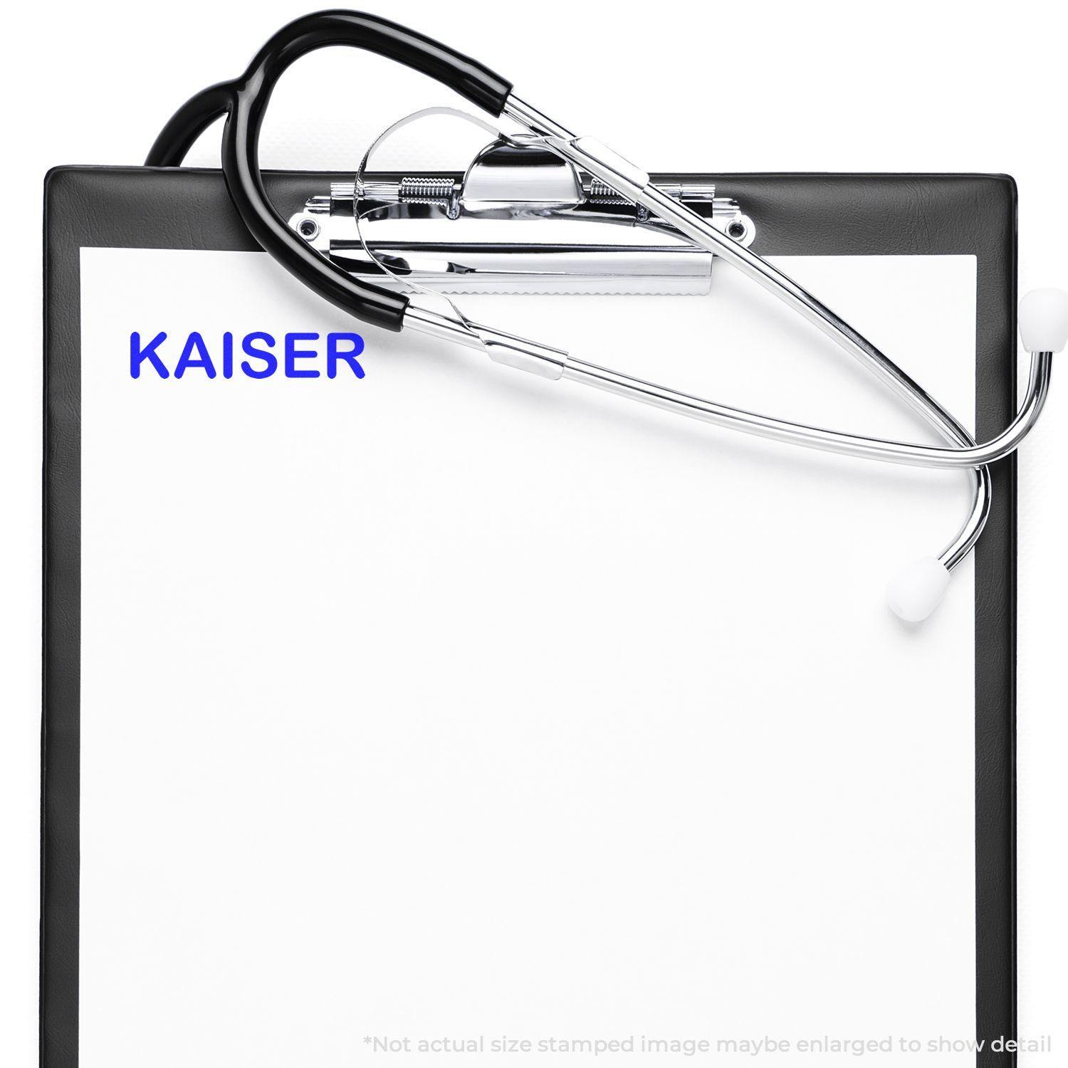 Slim Pre-Inked Kaiser Stamp used on a medical clipboard with a stethoscope, showing the word KAISER stamped in blue ink.