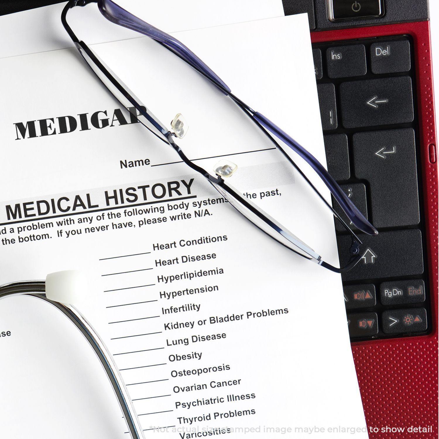 A Large Pre-Inked Medigap Stamp is placed on a medical history form, with a stethoscope and glasses nearby on a keyboard.