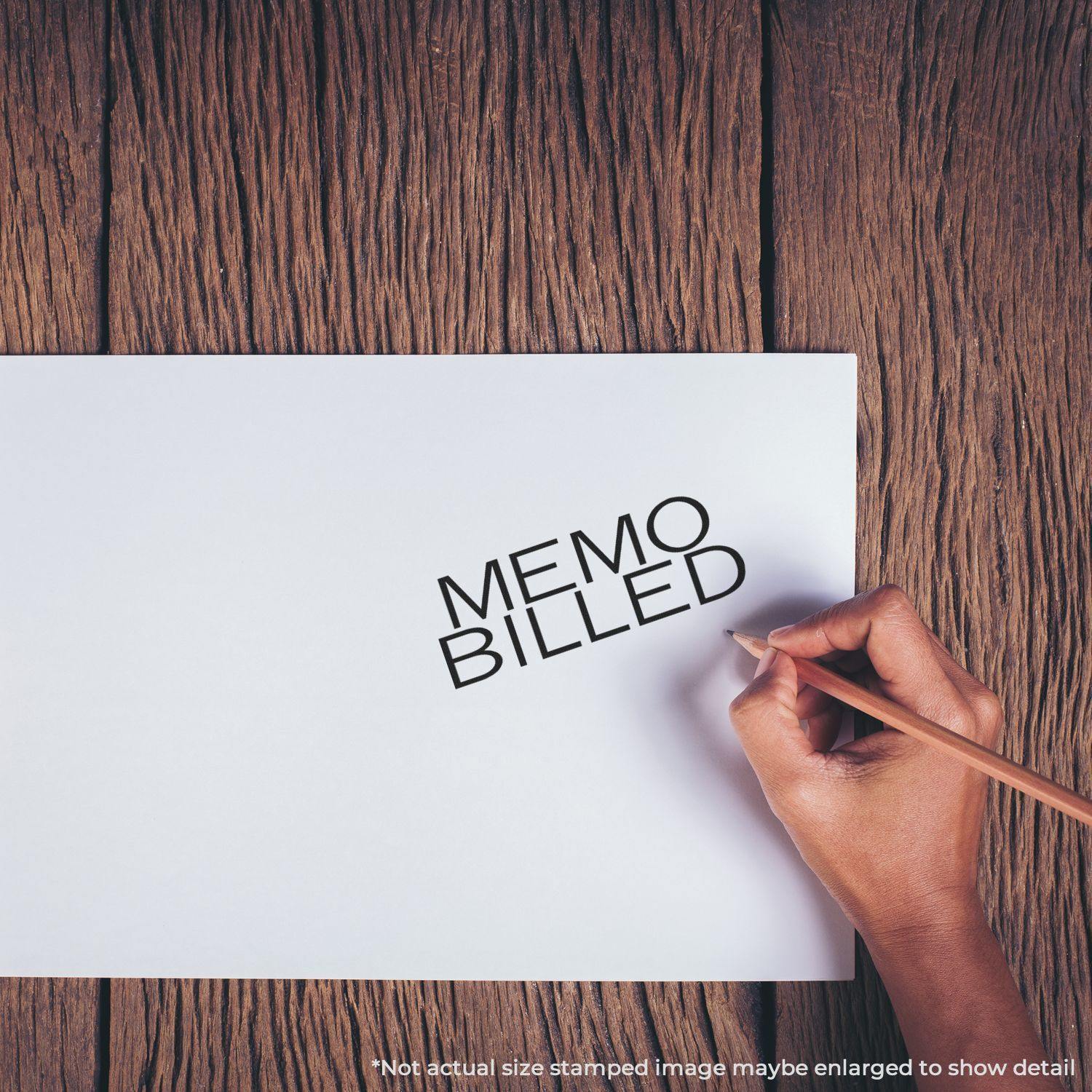 Hand using Large Memo Billed Rubber Stamp on white paper, with MEMO BILLED text stamped in black ink on a wooden surface background.