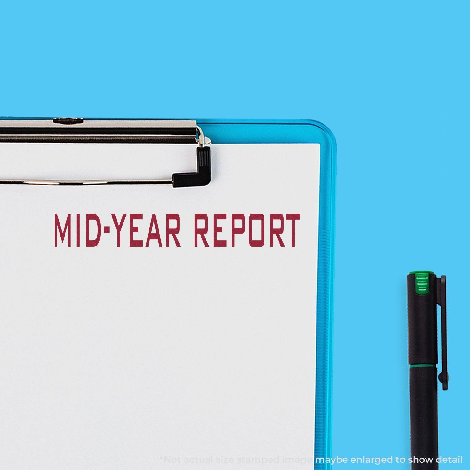 Clipboard with a stamped Mid-Year Report in red ink, next to a black and green pen on a blue background.