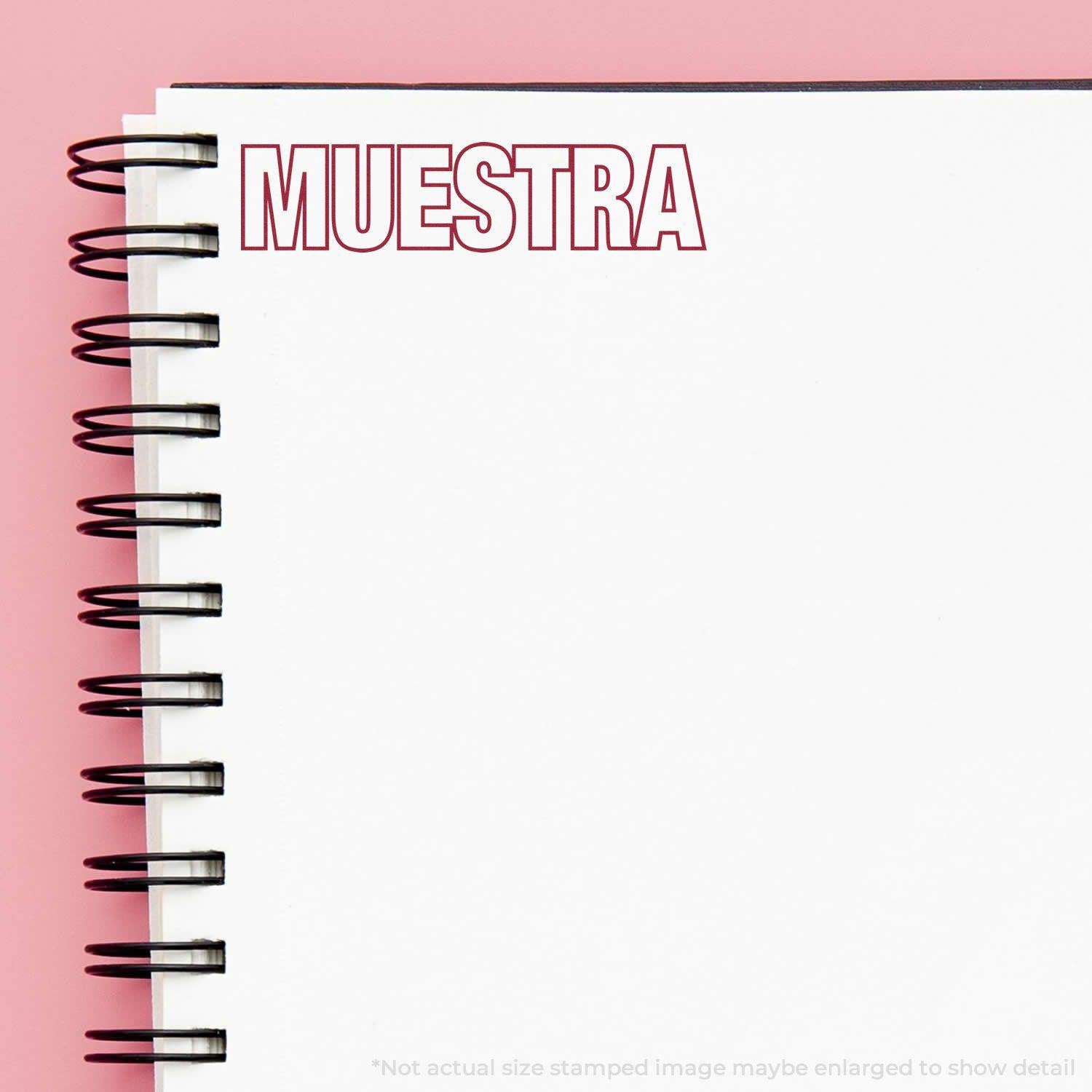 Large Muestra Rubber Stamp imprint in red ink on a white spiral notebook with a pink background.