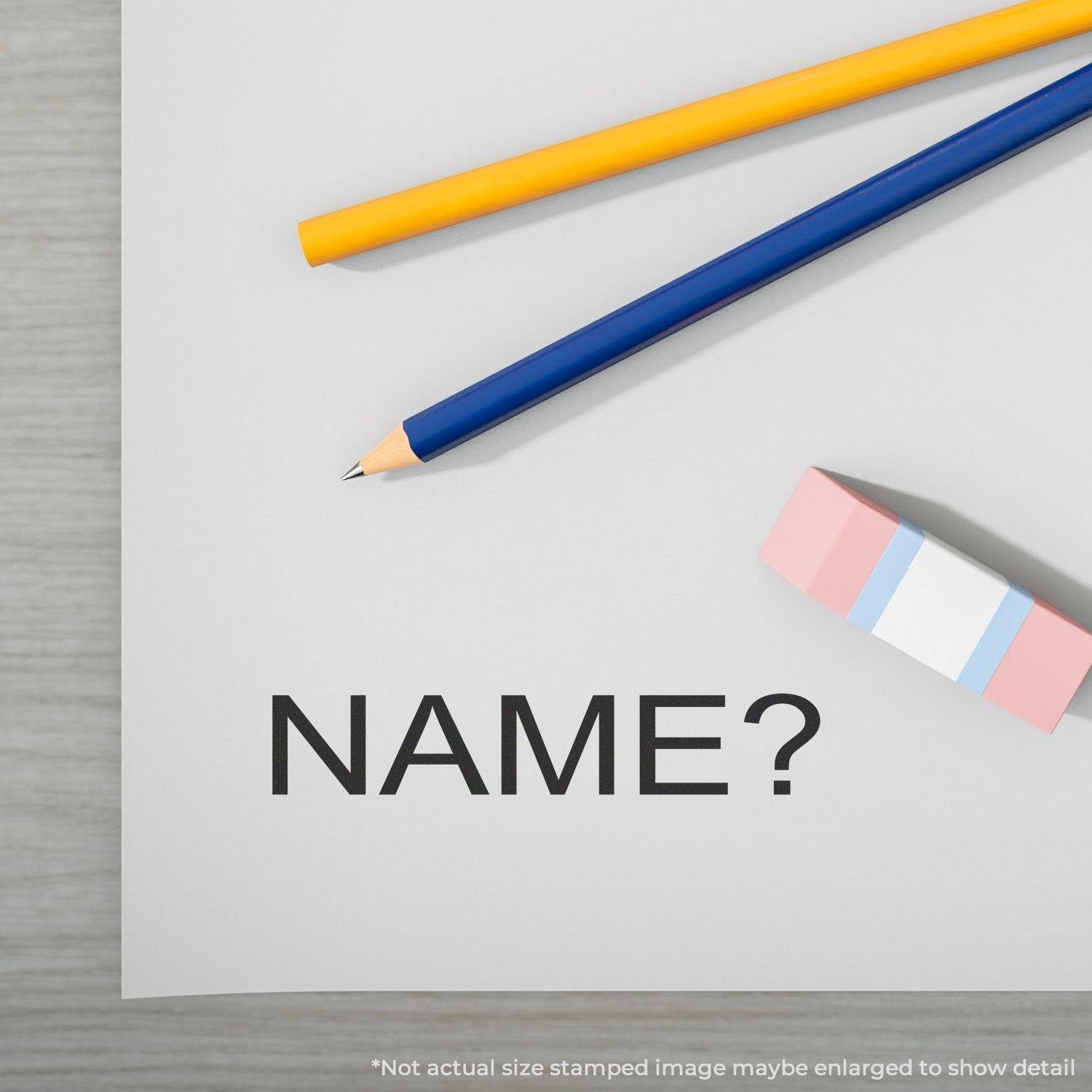 A name rubber stamp is shown on a paper with the word NAME? next to a pencil, pen, and eraser on a wooden surface.