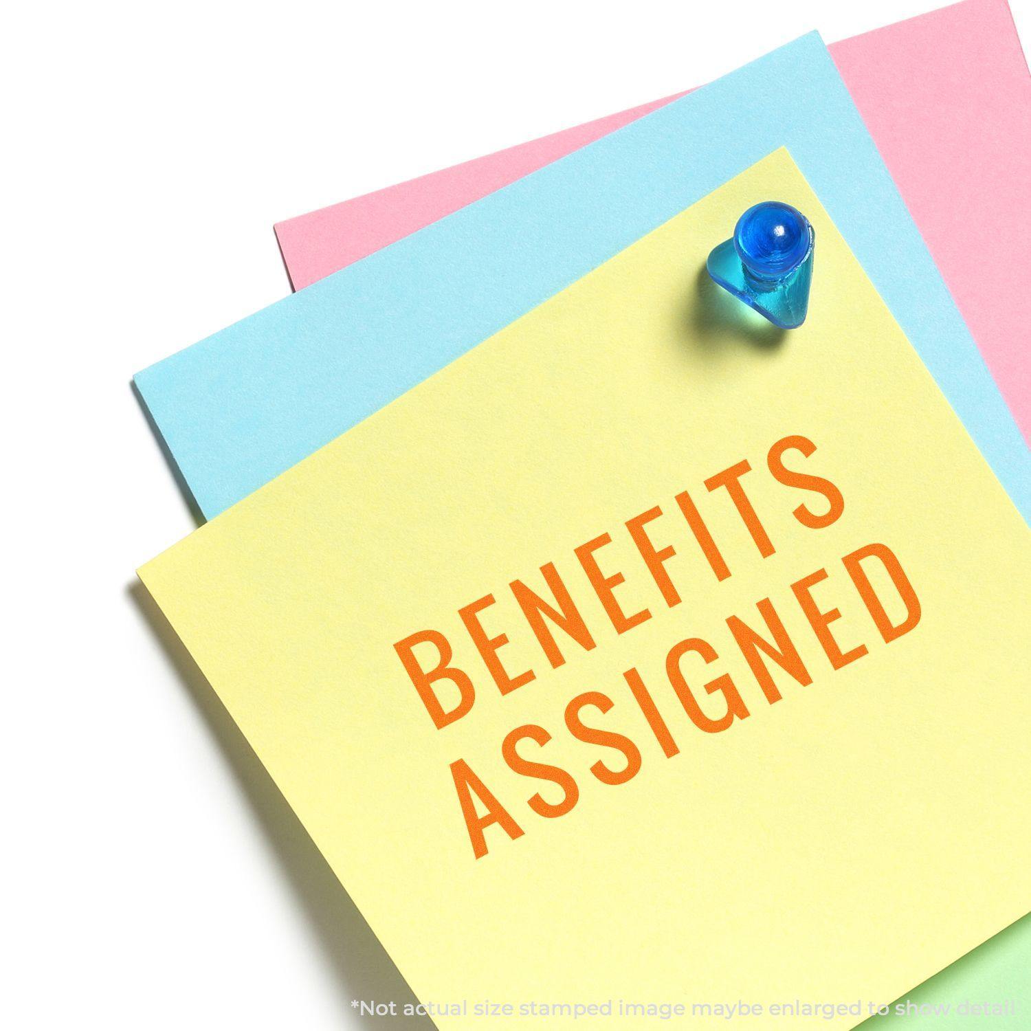 Slim Pre-Inked Narrow Benefits Assigned Stamp marking BENEFITS ASSIGNED on a yellow sticky note pinned to a board.