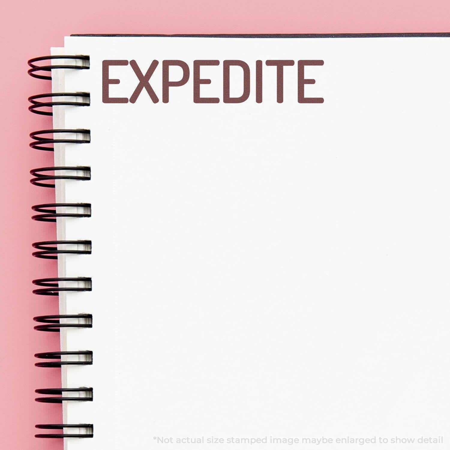 A stock office rubber stamp with a stamped image showing how the text "EXPEDITE" in a large narrow font is displayed after stamping.