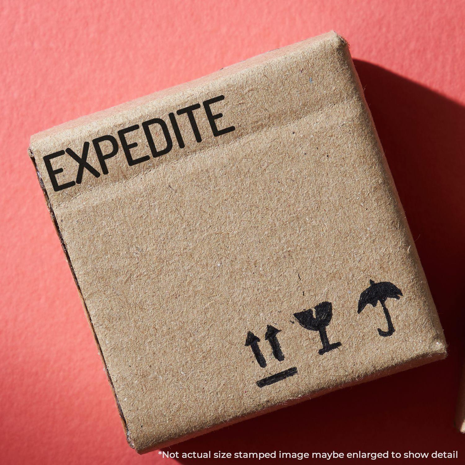 Cardboard box stamped with EXPEDITE using the Large Self Inking Narrow Expedite Stamp, placed on a red surface.