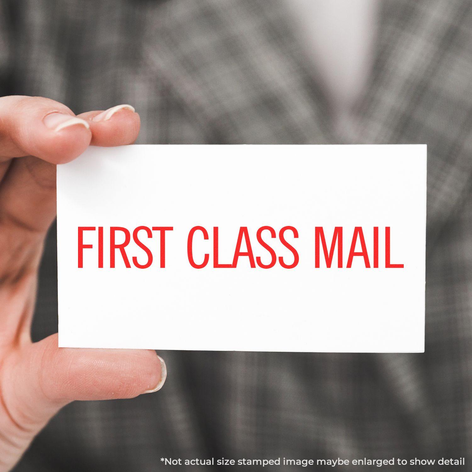 Person holding a white card stamped with FIRST CLASS MAIL in red using a narrow first class mail rubber stamp.