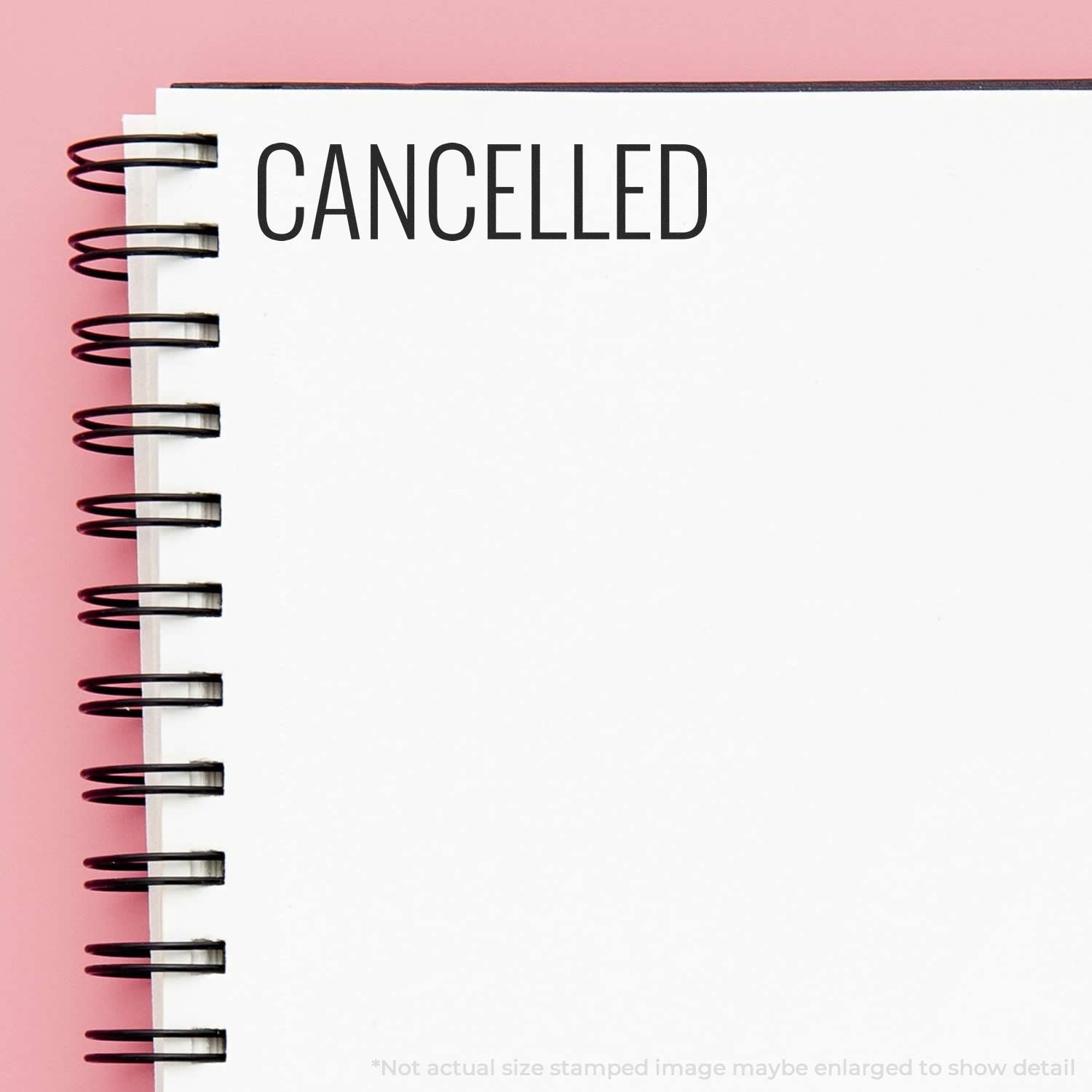 Self Inking Narrow Font Cancelled Stamp used on a white spiral notebook, showing the word CANCELLED in black ink on a pink background.