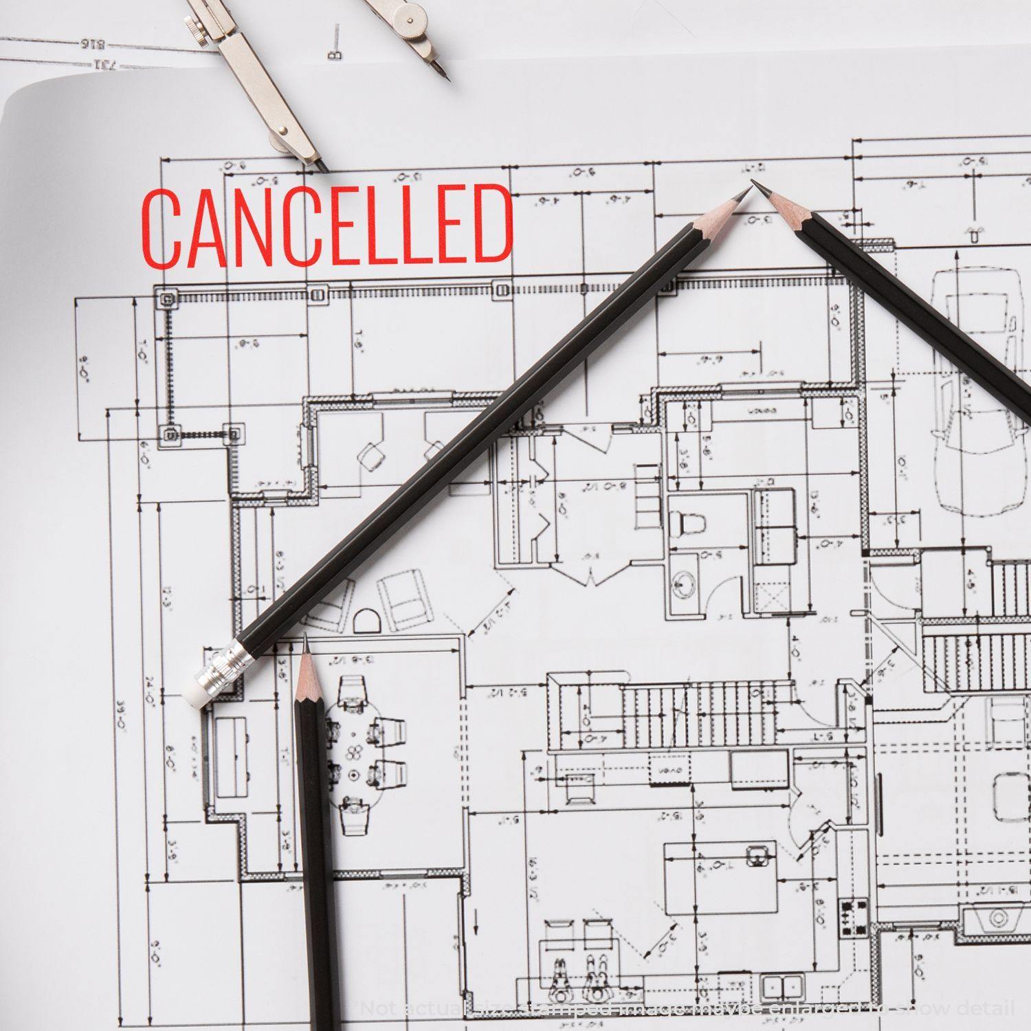 Architectural blueprint with Cancelled stamped in red narrow font, surrounded by pencils and a compass.