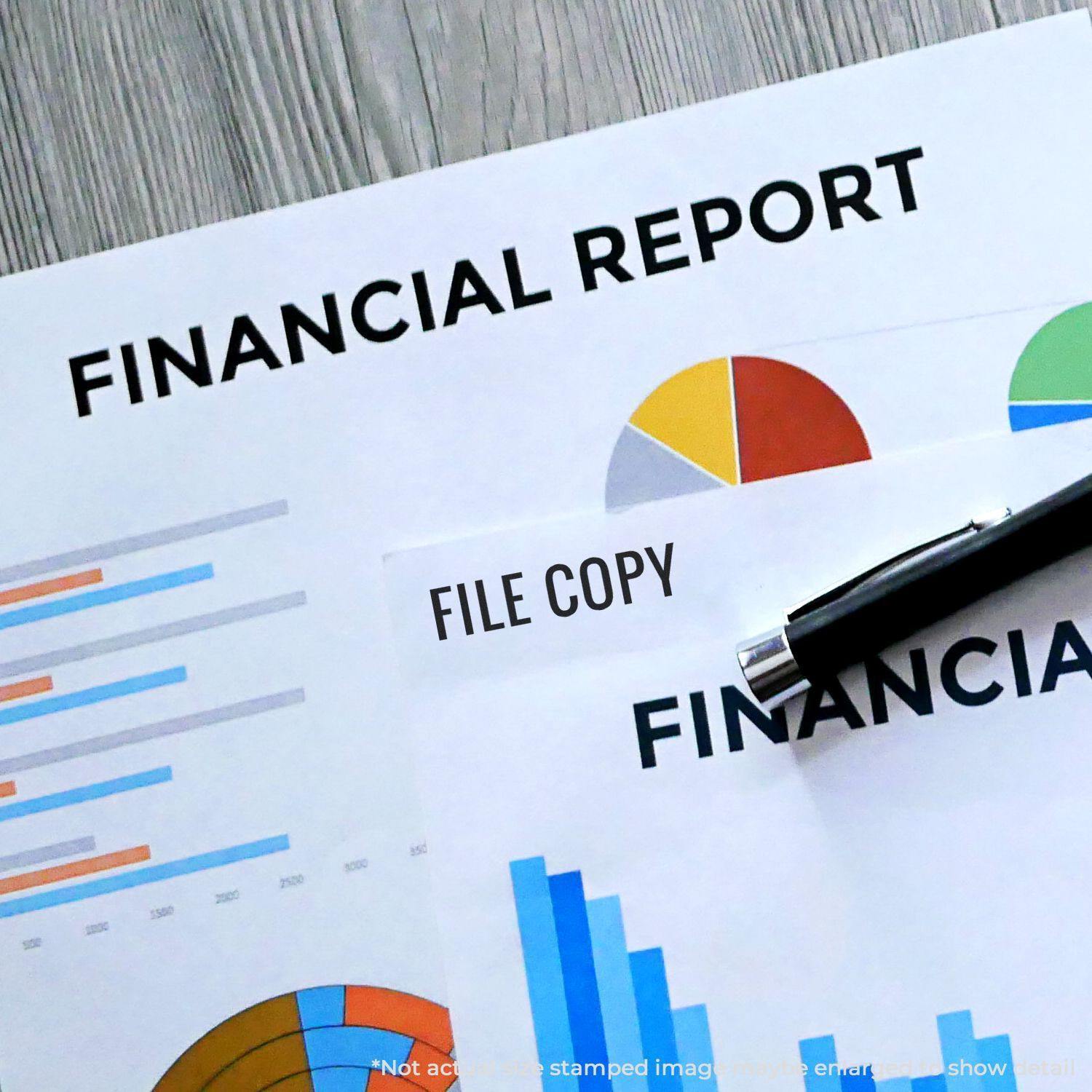 Slim Pre-Inked Narrow Font File Copy Stamp used on financial report documents with charts and graphs on a wooden desk.