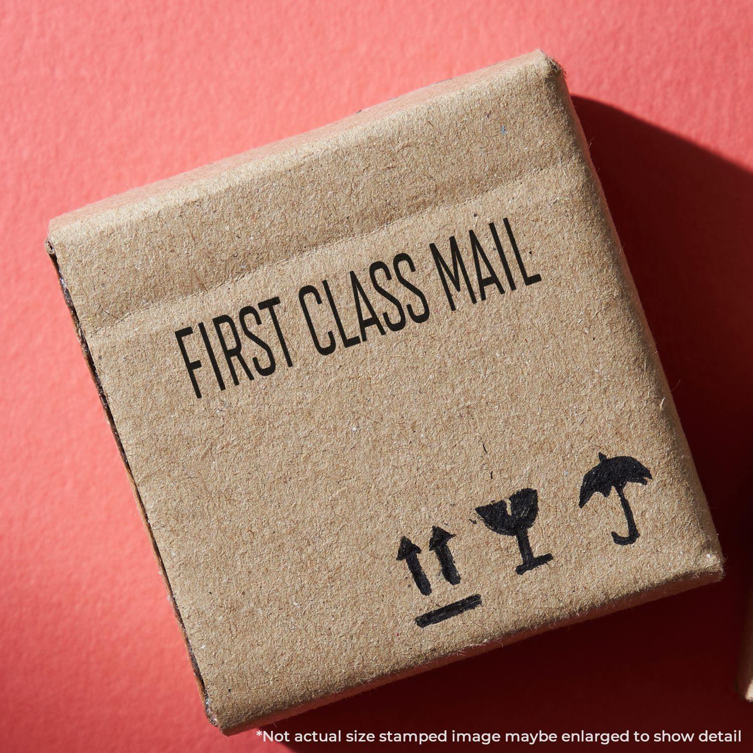 Narrow Font First Class Mail rubber stamp on a small brown cardboard box with shipping symbols, against a red background.