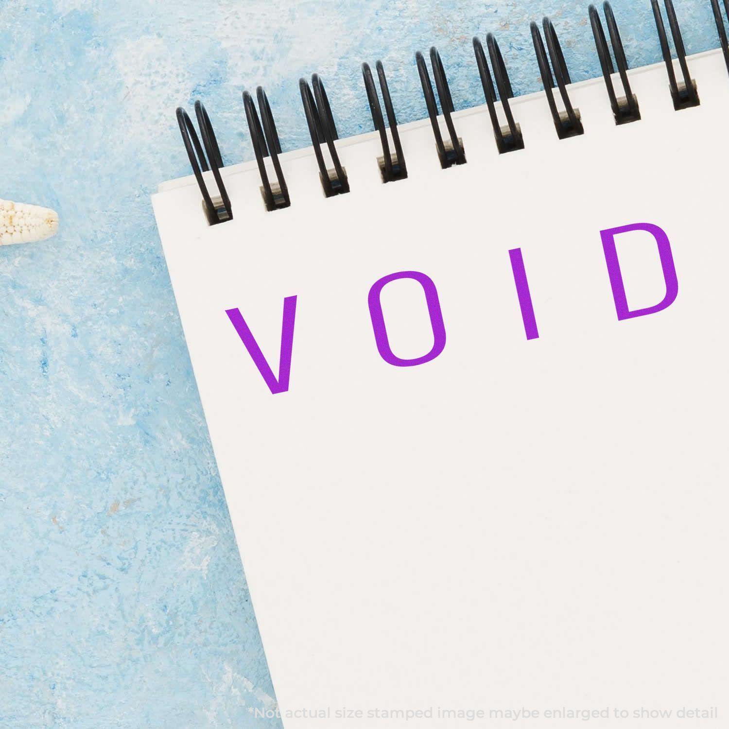 Large Narrow Void Rubber Stamp used on a white notepad, displaying the word VOID in purple ink against a blue background.