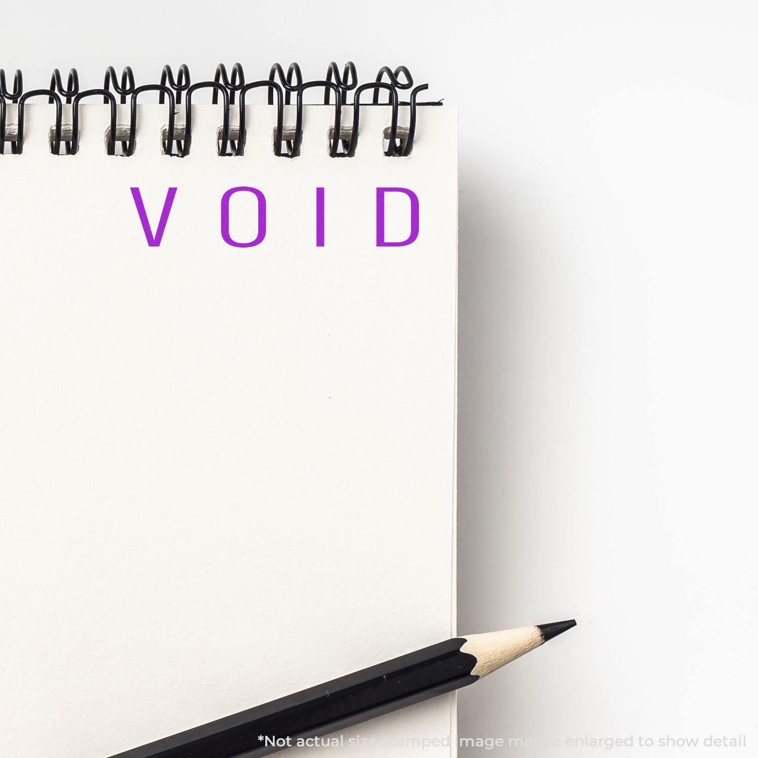 Large Narrow Void Rubber Stamp imprinting VOID in purple ink on a white notepad, with a black pencil placed beside the notepad.