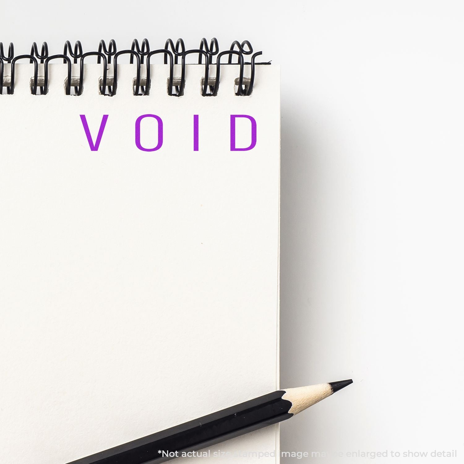 Self Inking Narrow Void Stamp imprinting VOID in purple ink on a white notepad with a black pencil beside it.