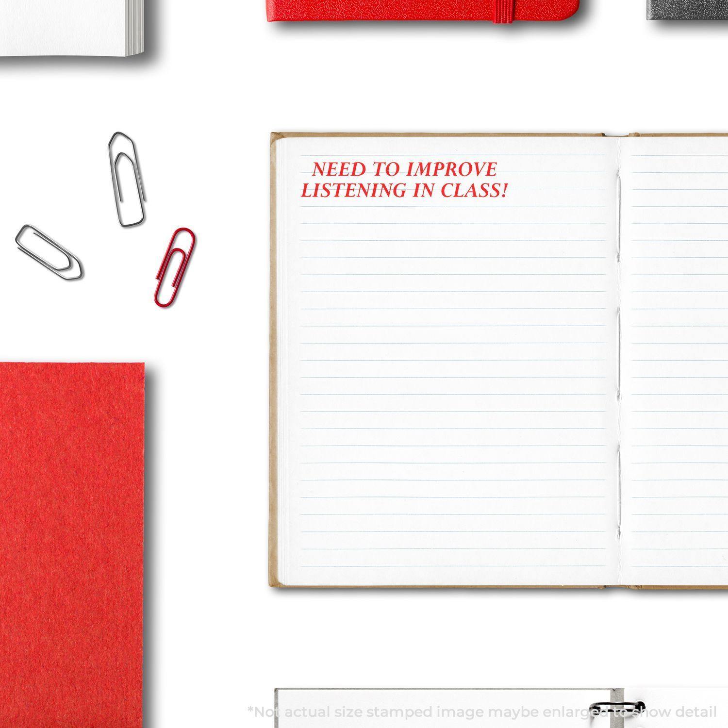 Open notebook with Need To Improve Listening In Class rubber stamp in red ink, surrounded by paperclips and red stationery.