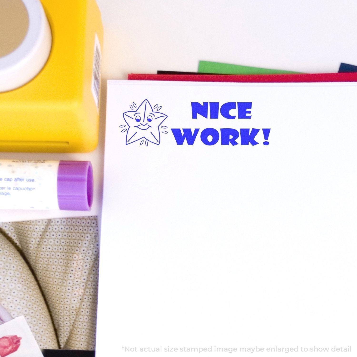 A stock office rubber stamp with a stamped image showing how the text "NICE WORK!" in a large bold font with an image of a smiling starfish on the left side is displayed after stamping.