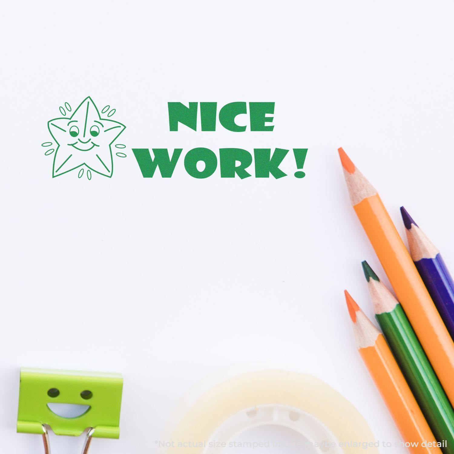 Nice Work rubber stamp impression with a smiling star, next to colored pencils, a green binder clip, and tape on a white surface.