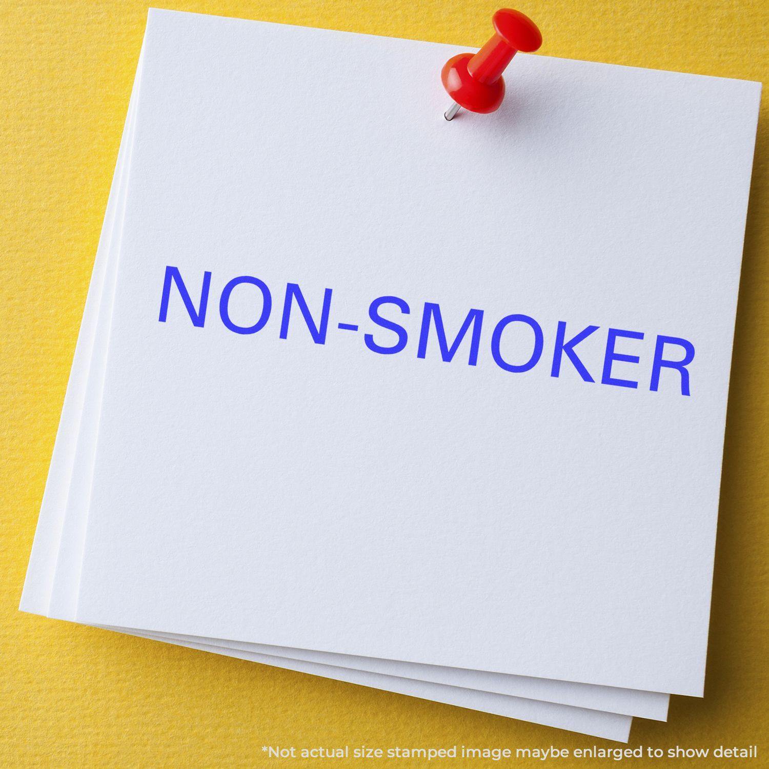 A stack of white papers stamped with NON-SMOKER in blue ink using the Large Non-Smoker Rubber Stamp, pinned with a red pushpin.