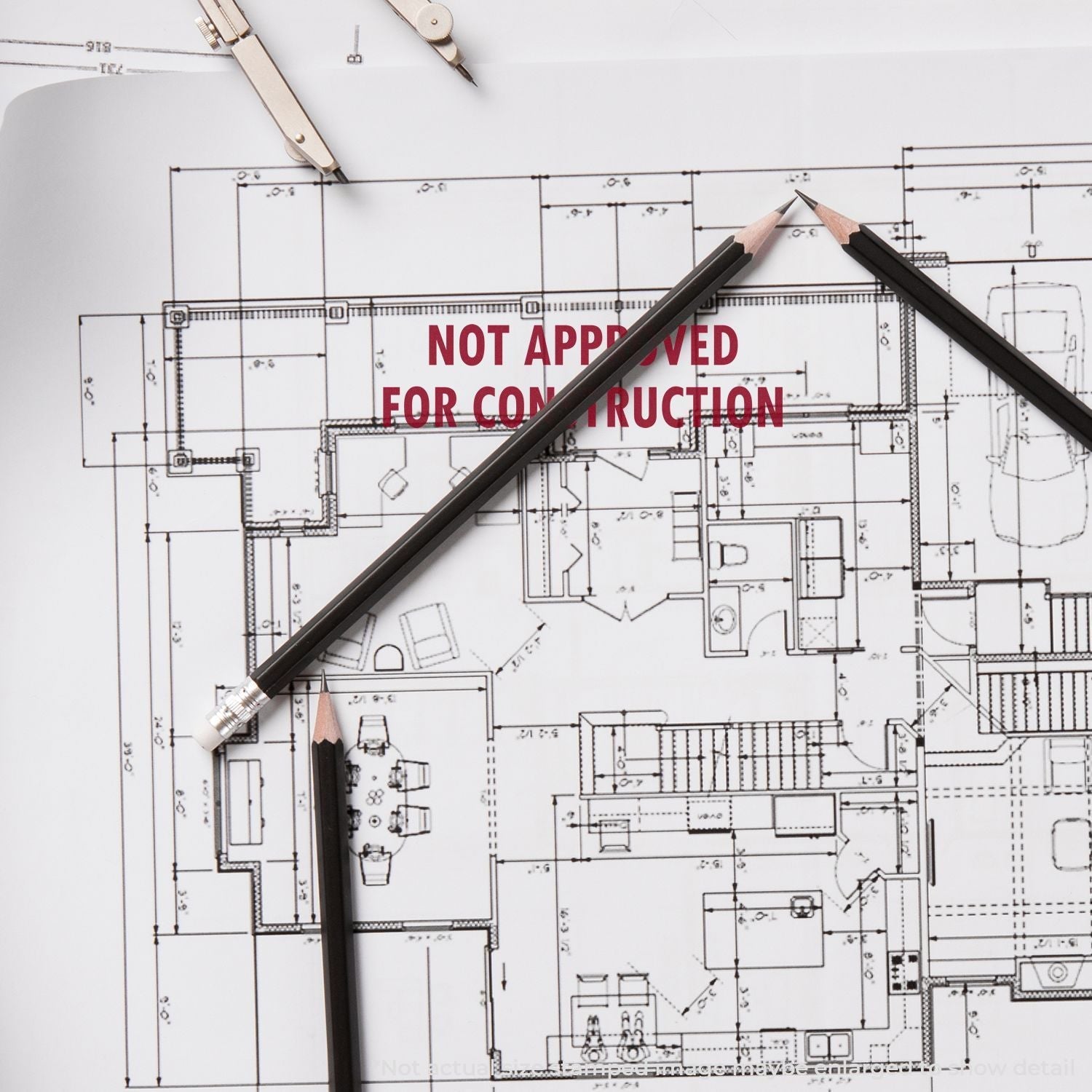 Architectural blueprint with a Self Inking Not Approved For Construction Stamp mark, surrounded by pencils and drafting tools.