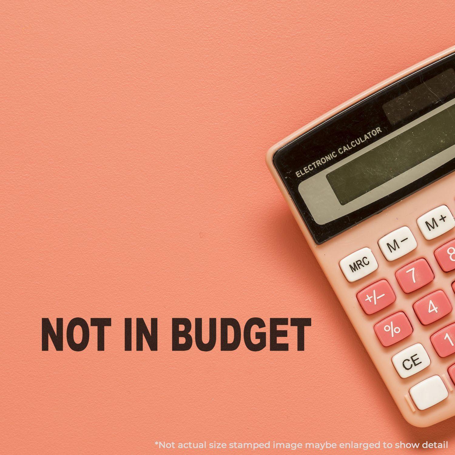 Large Self Inking Not In Budget Stamp impression on a peach background next to a pink calculator.