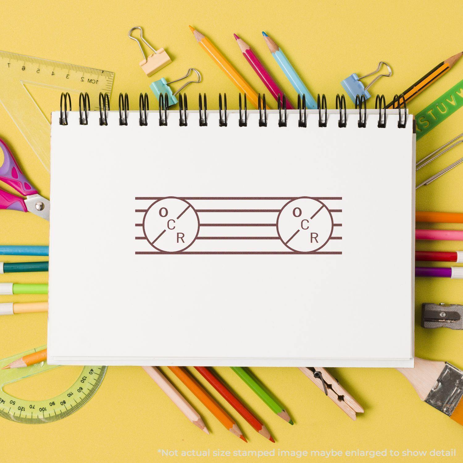 A notebook with an OCR Rubber Stamp impression on a desk surrounded by colorful stationery items against a yellow background.