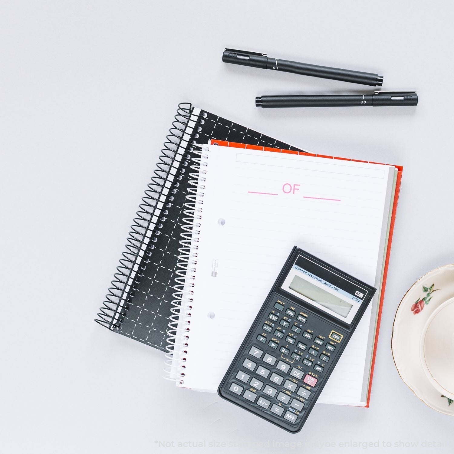 Self Inking Pkg Of Stamp used on a notebook, with pens, a calculator, and a teacup on a white desk.