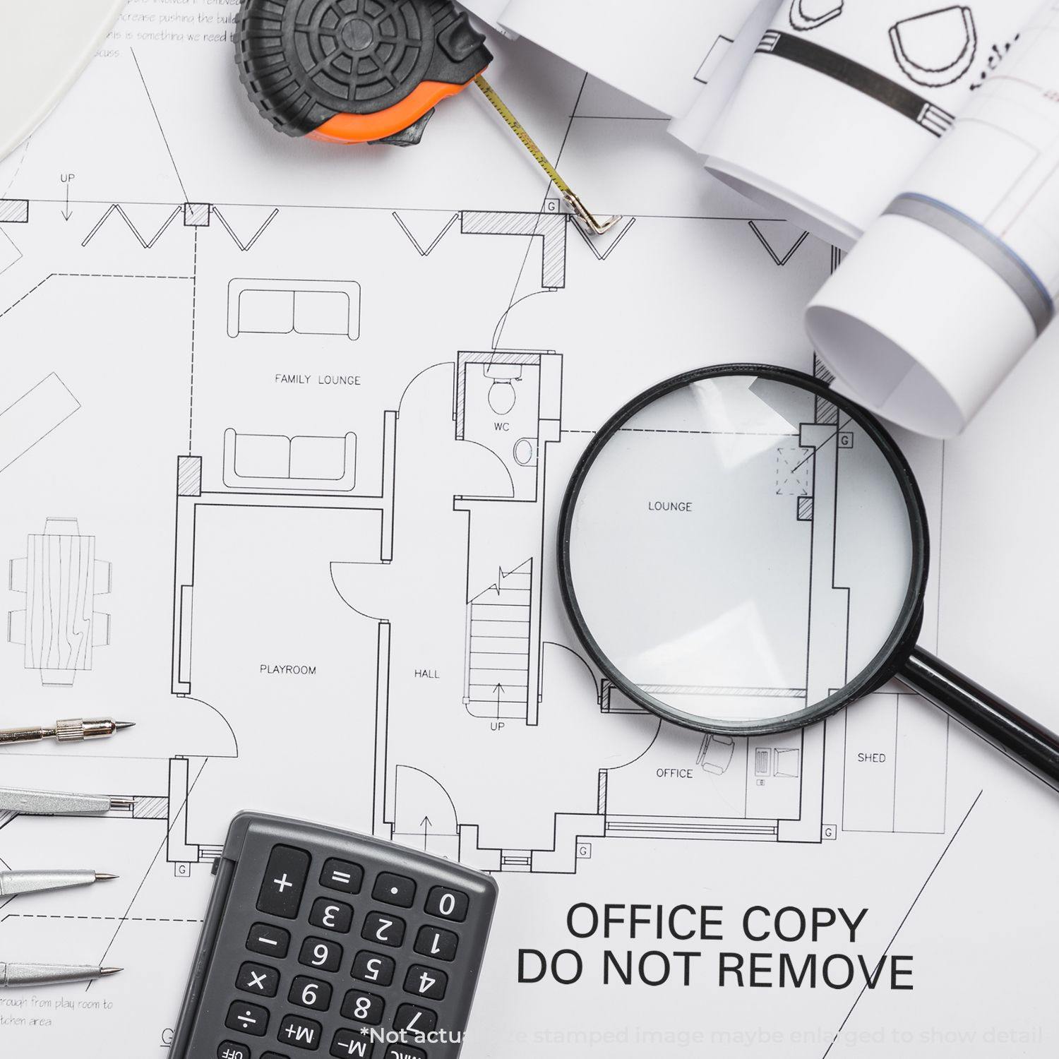 Large Self Inking Office Copy Do Not Remove Stamp on architectural plans with a magnifying glass, calculator, and measuring tape.