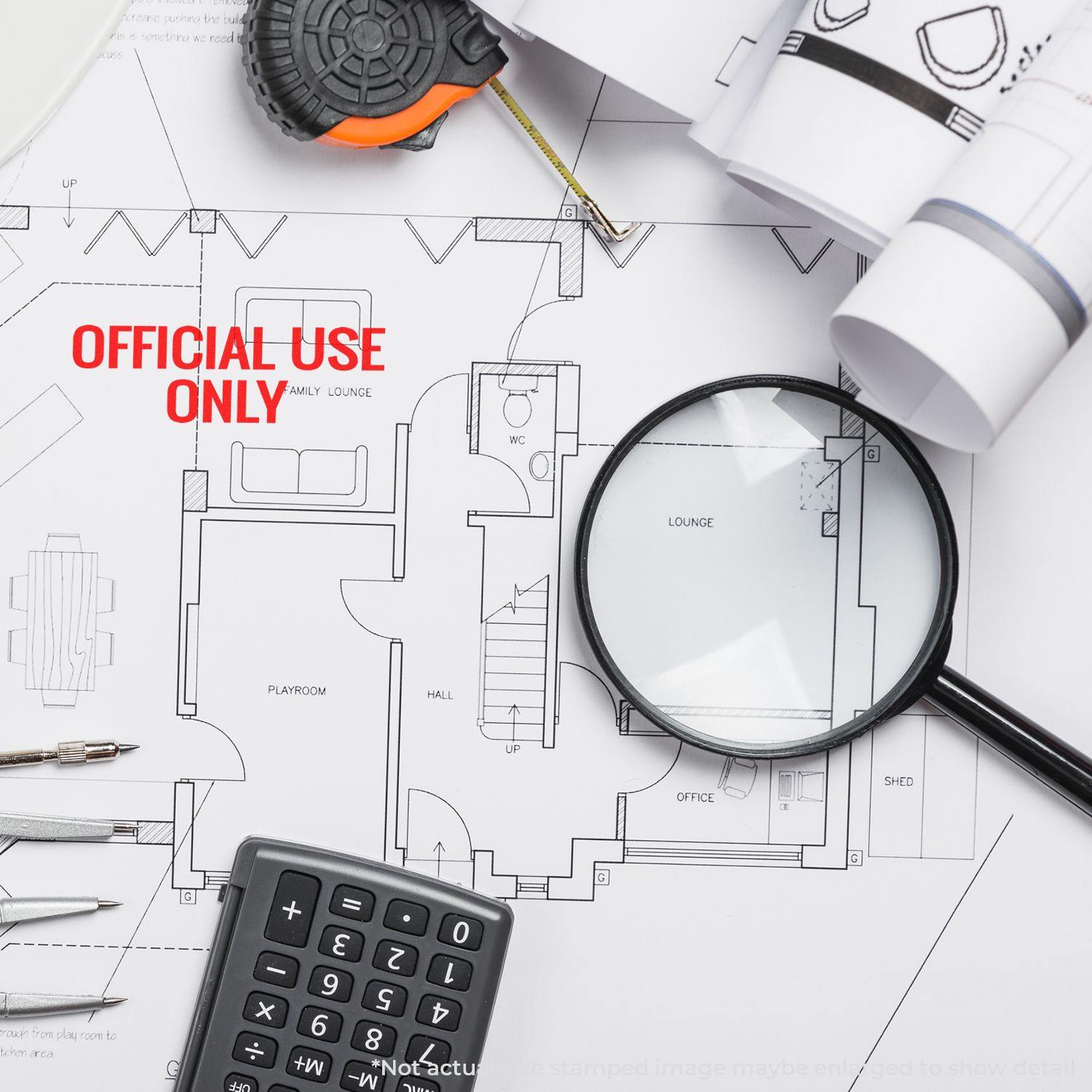 A Large Self Inking Official Use Only Stamp on a blueprint with a magnifying glass, calculator, tape measure, and pens.