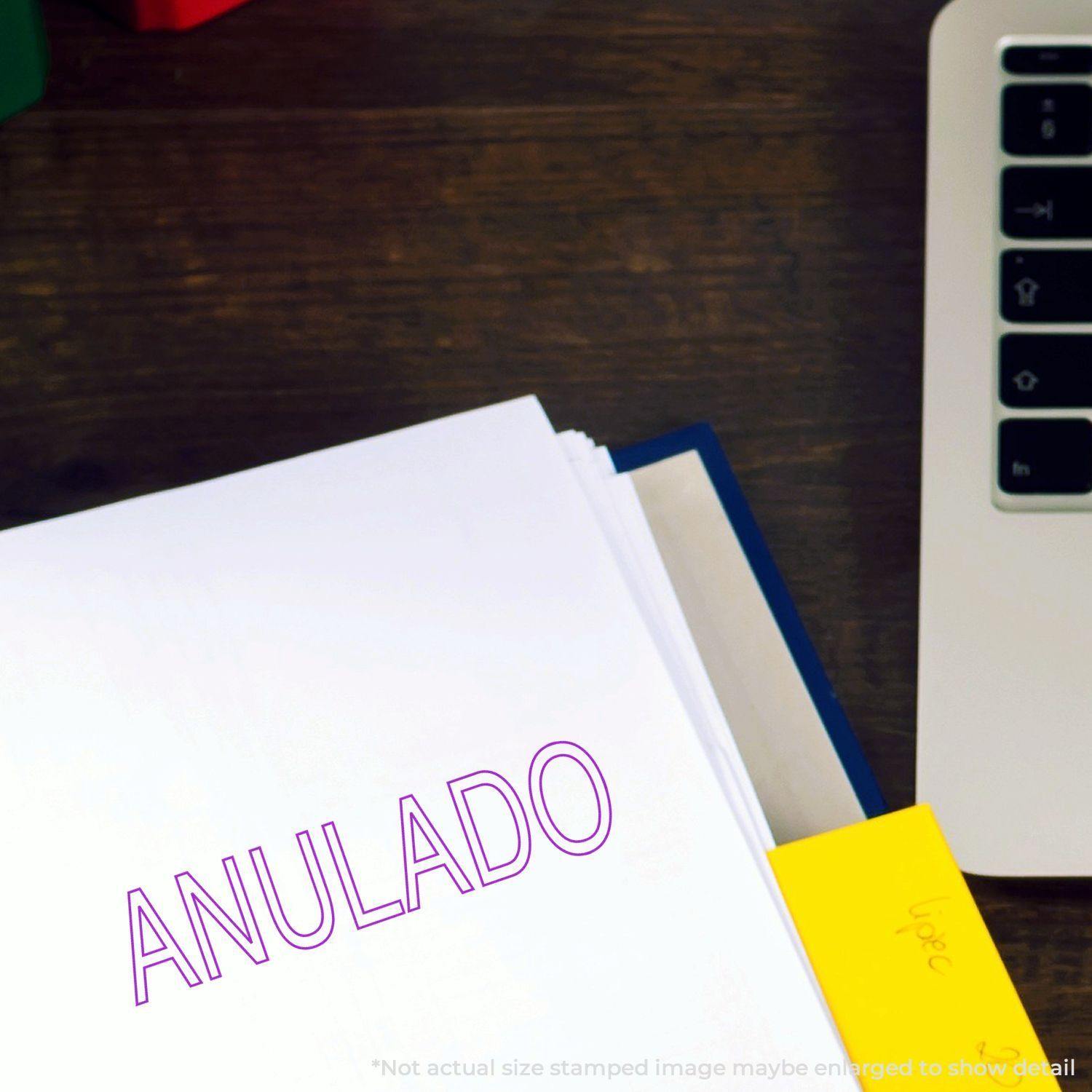 Outline Anulado Rubber Stamp in purple ink on a white document next to a laptop and a yellow sticky note on a wooden desk.