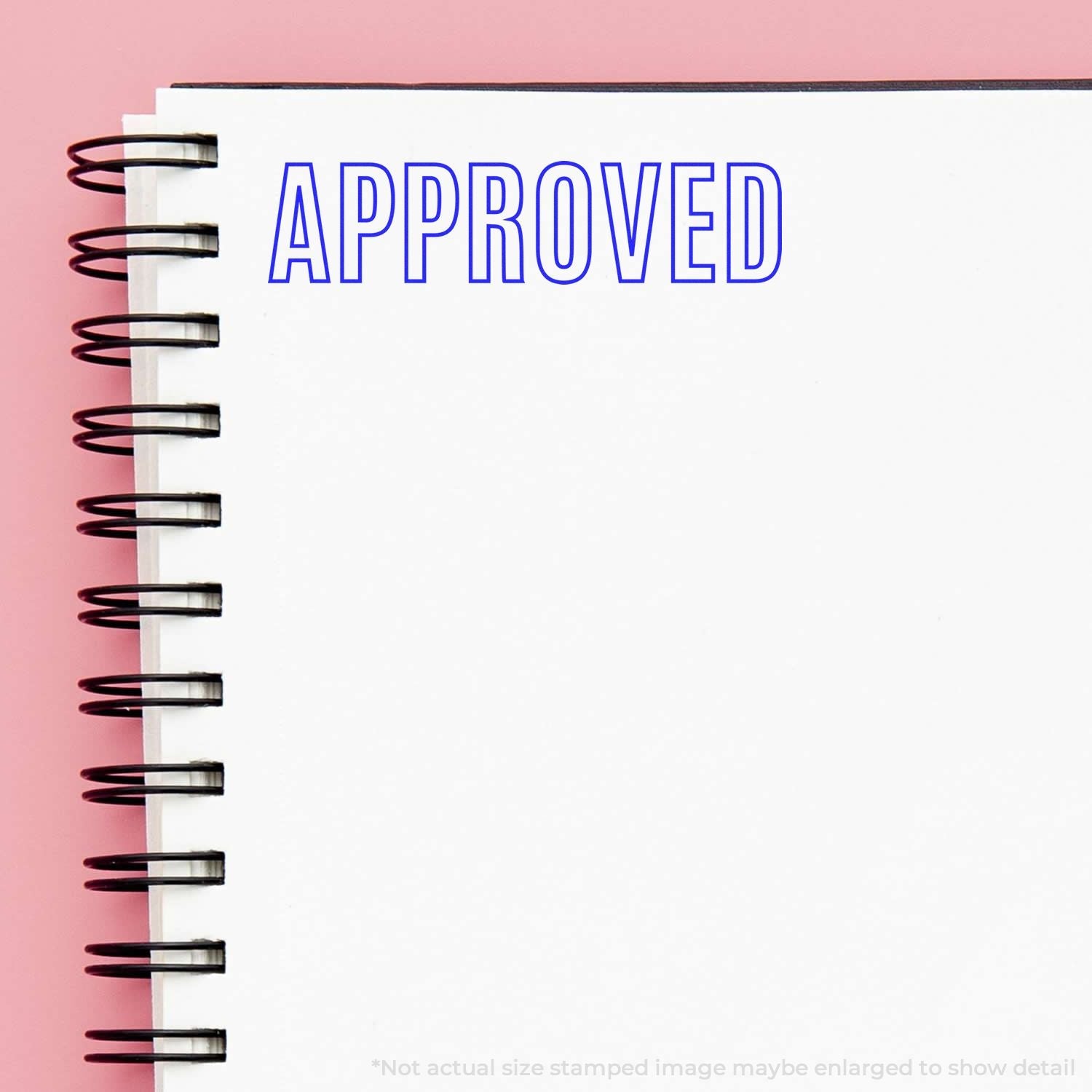 Self Inking Outline Approved Stamp marking APPROVED in blue ink on a white spiral notebook against a pink background.