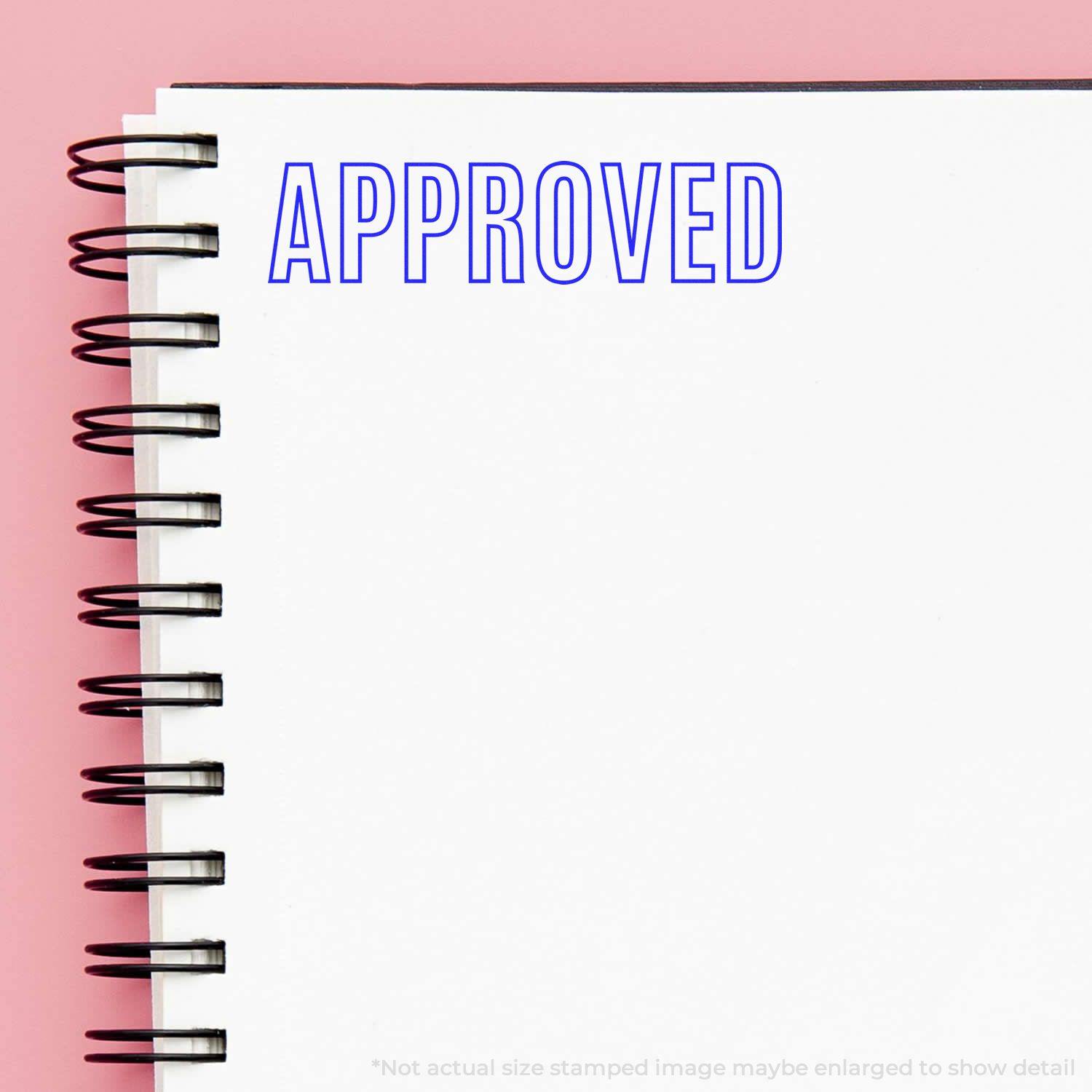 A notebook with a spiral binding and a blue "APPROVED" stamp using the Outline Approved Rubber Stamp on a pink background.