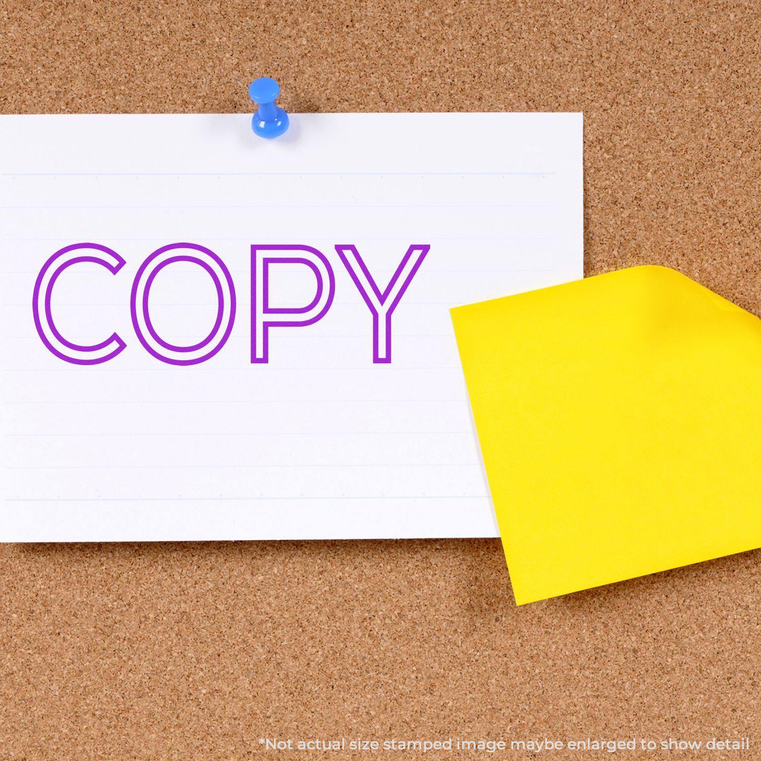 Large Self Inking Outline Copy Stamp in purple ink on a white note pinned to a corkboard, with a yellow sticky note partially visible.