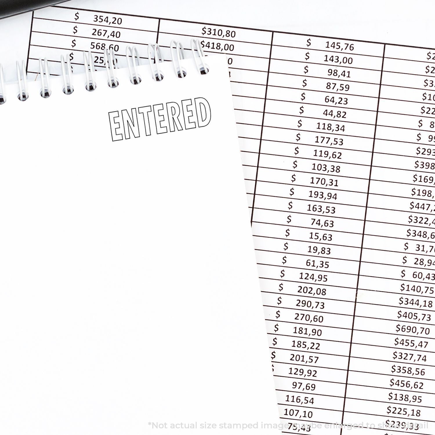 Self Inking Outline Entered Stamp used on a notebook page with the word ENTERED stamped, next to a financial spreadsheet.