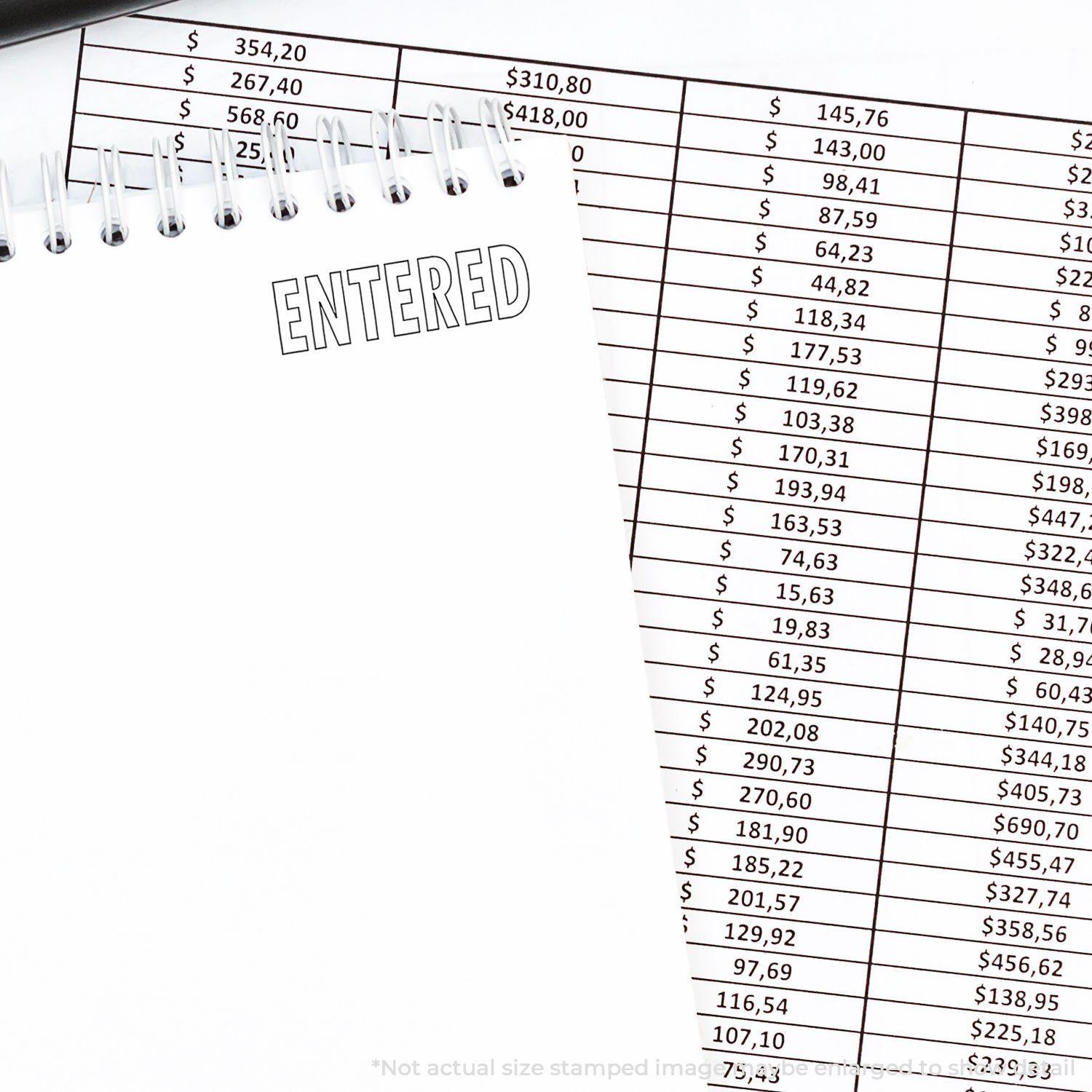 Notebook with Entered stamped in outline next to a financial spreadsheet. Focus on Outline Entered Rubber Stamp.