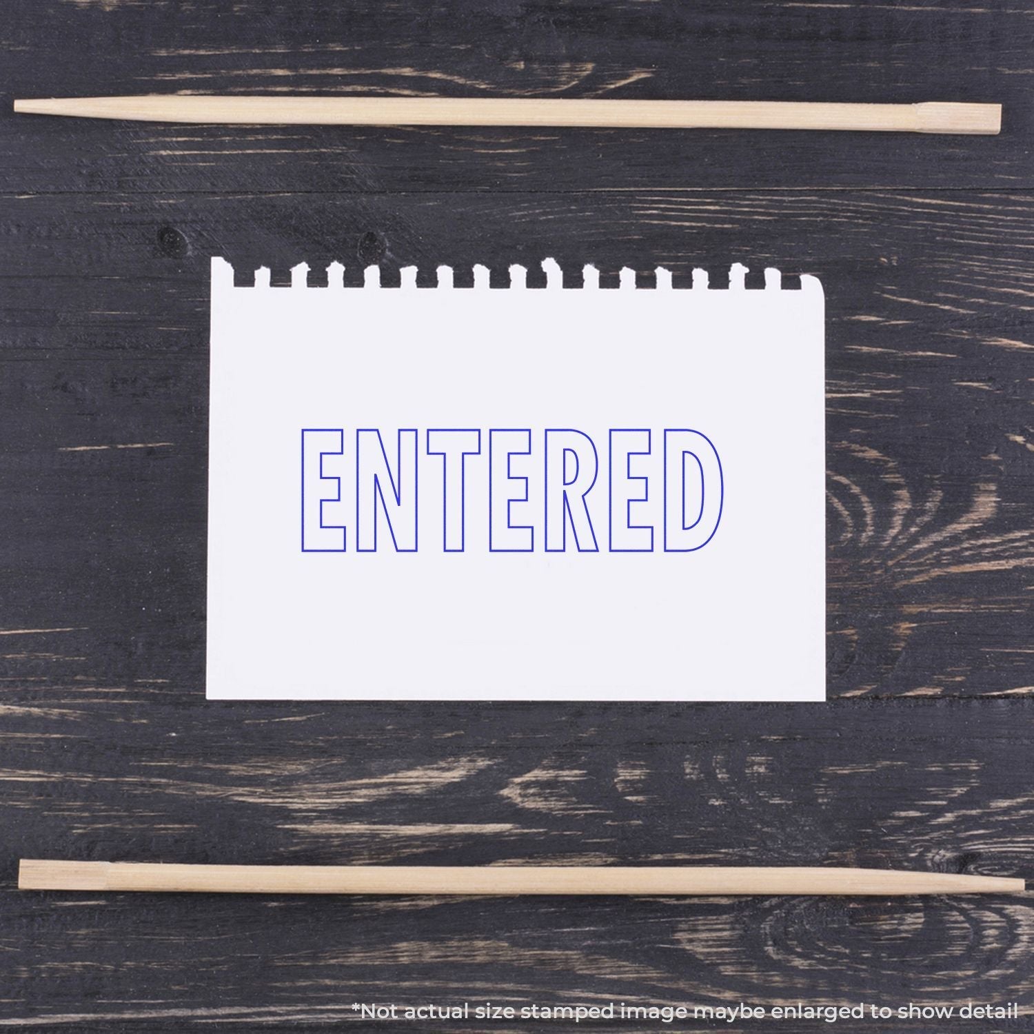 Self Inking Outline Entered Stamp used on a white notepad, displaying the word ENTERED in blue ink, placed on a dark wooden surface.