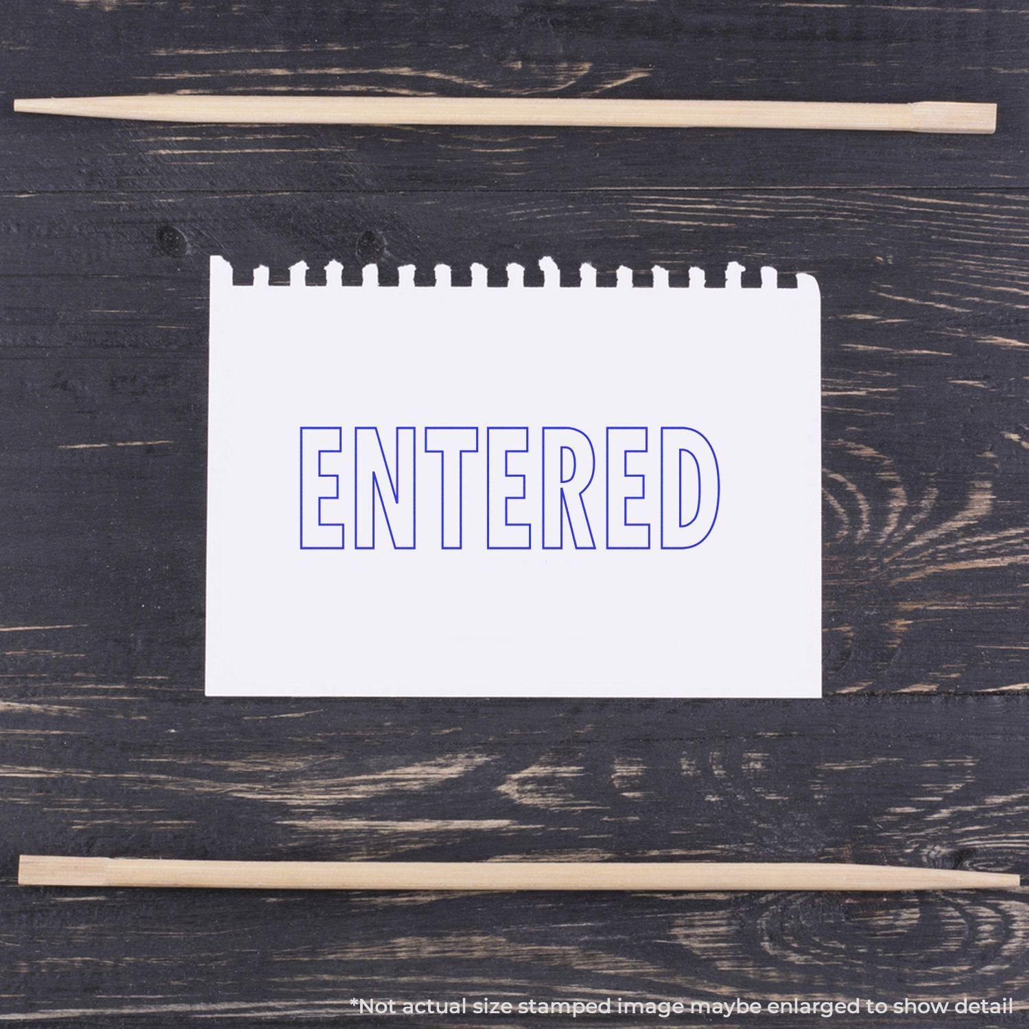 Large Self Inking Entered Stamp Outline Text on a white notepad with wooden sticks on a dark wooden surface.