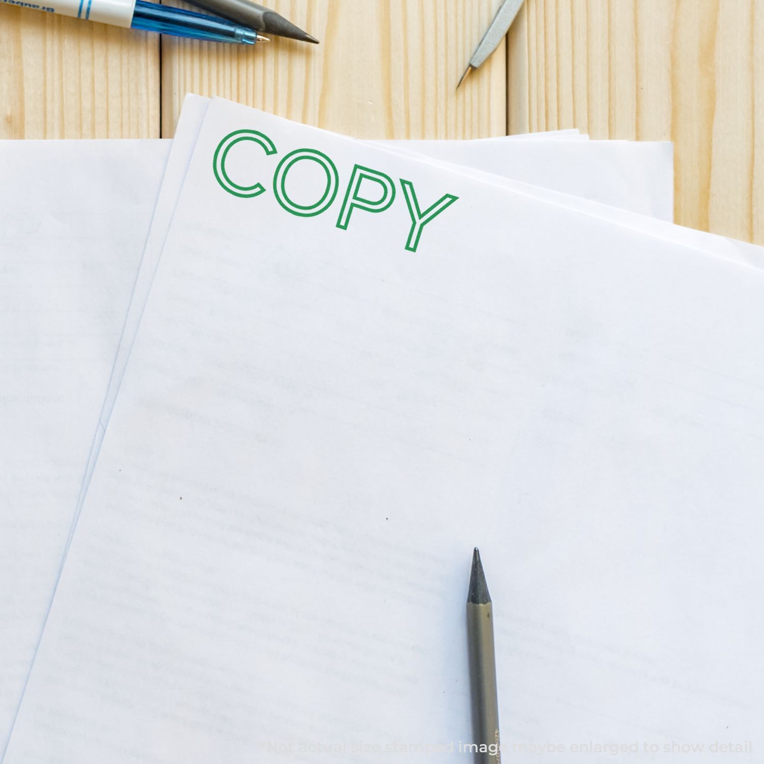 Self Inking Outline Font Copy Stamp marking the word COPY in green on a stack of white papers, with pens and a pencil on a wooden desk.