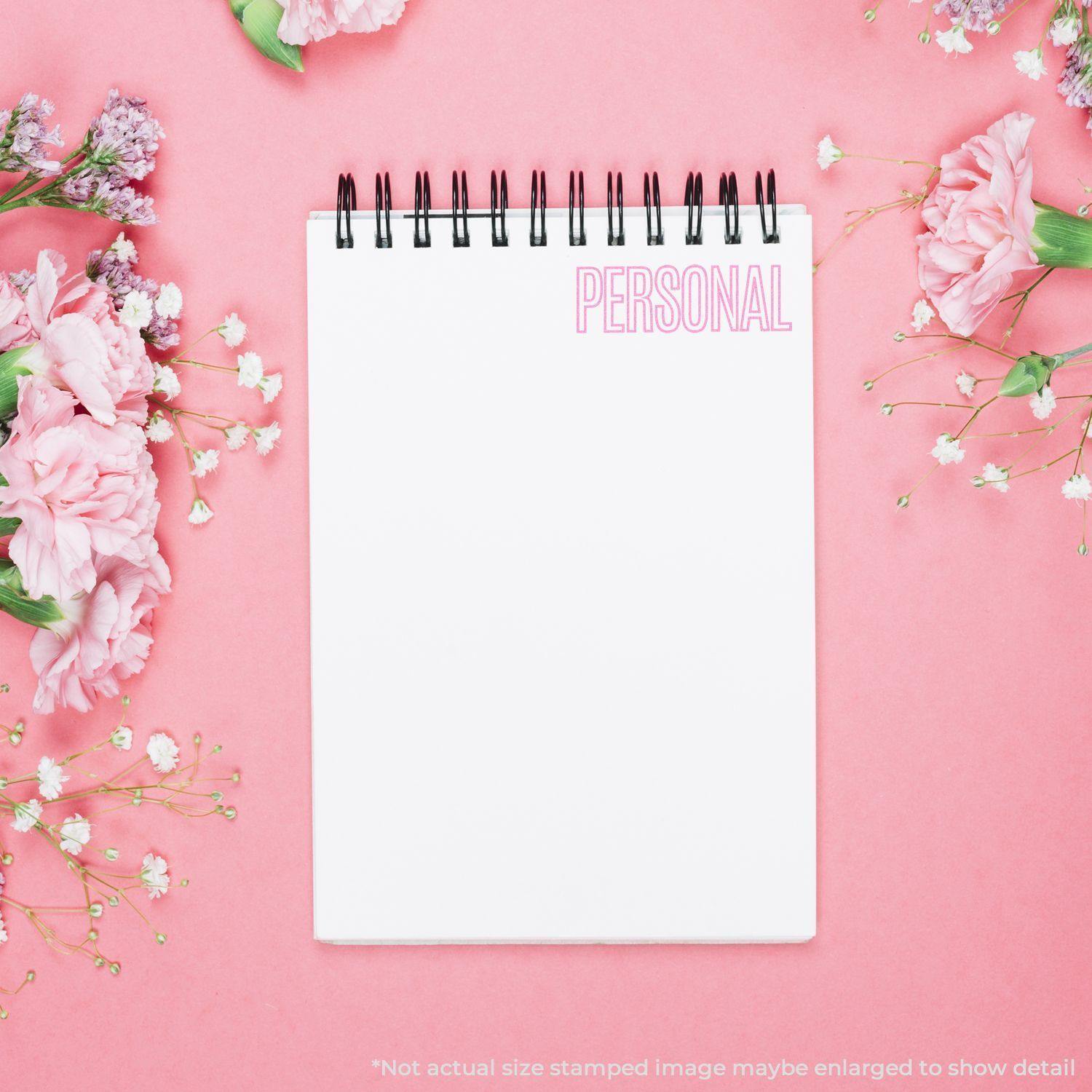 A Large Self Inking Outline Personal Stamp marks PERSONAL in pink on a white notepad, surrounded by pink and white flowers on a pink background.