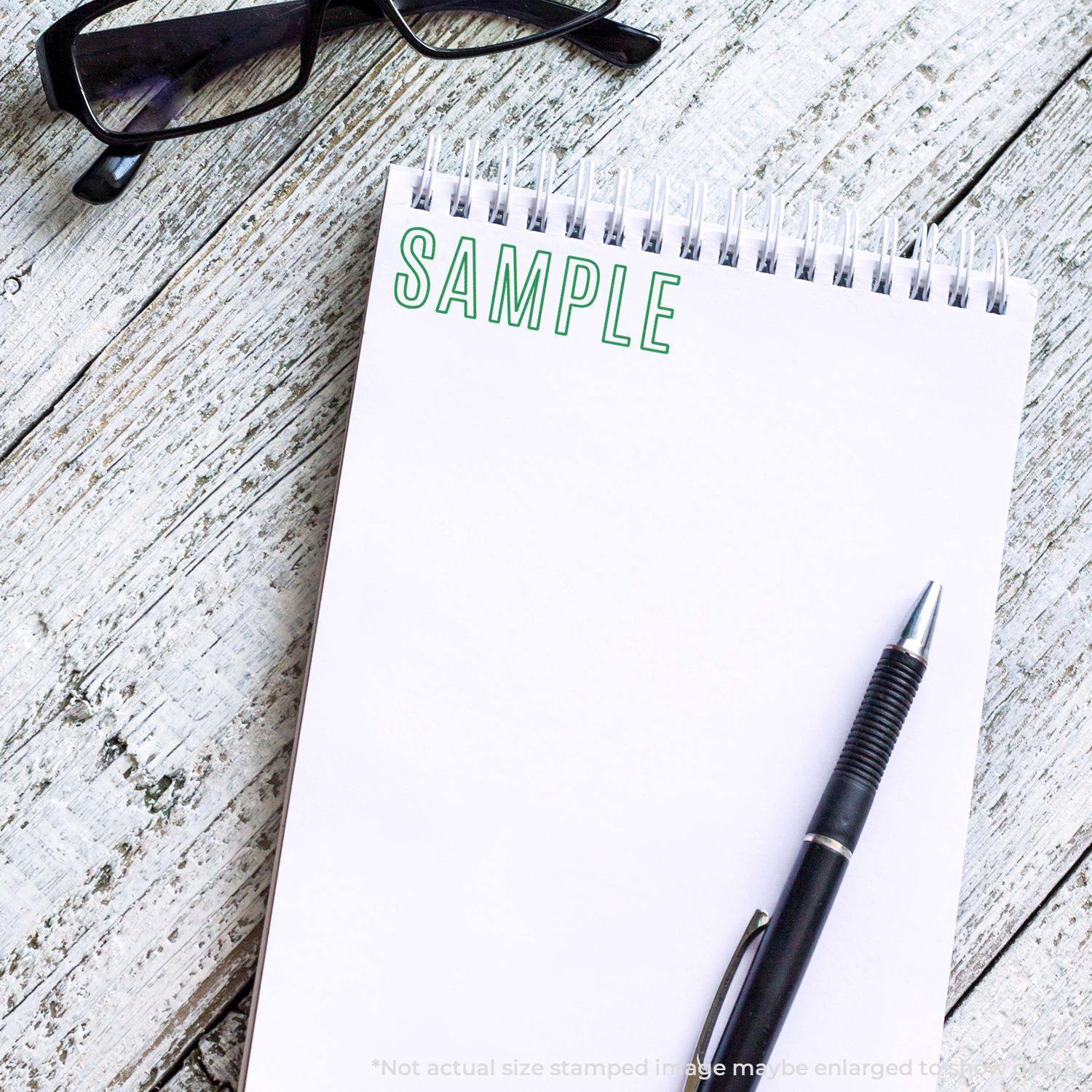 Slim Pre-Inked Outline Sample Stamp used on a white notepad with a pen and glasses on a wooden surface.