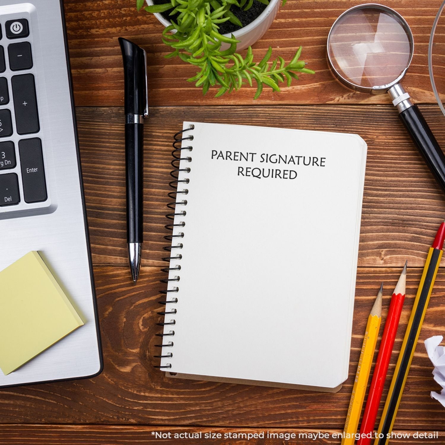 Self Inking Parent Signature Required Stamp on a notebook, surrounded by office supplies, a laptop, and a plant on a wooden desk.