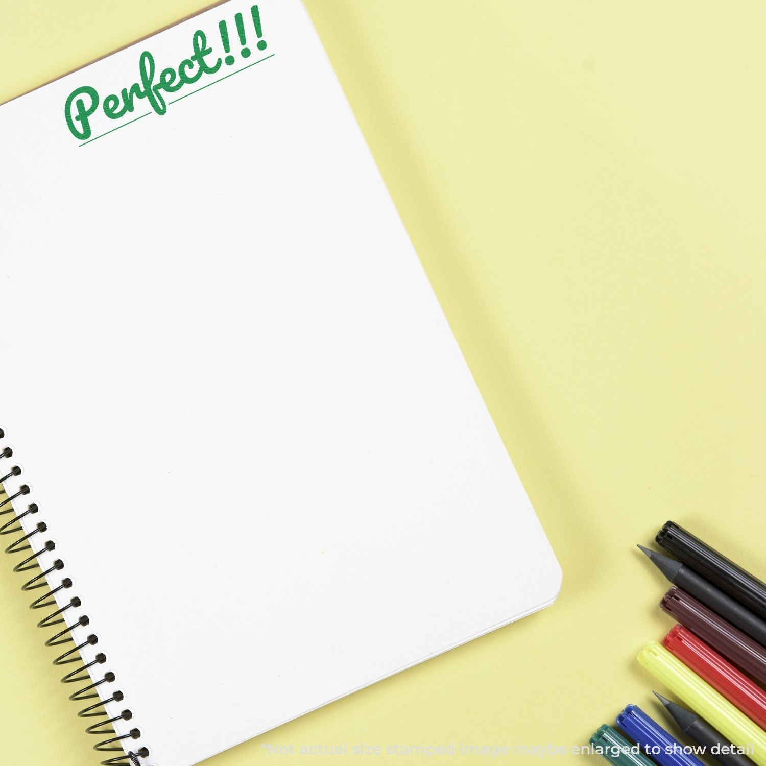 A Self Inking Perfect Stamp marks Perfect!!! in green ink on a white spiral notebook, surrounded by colorful pens and highlighters.