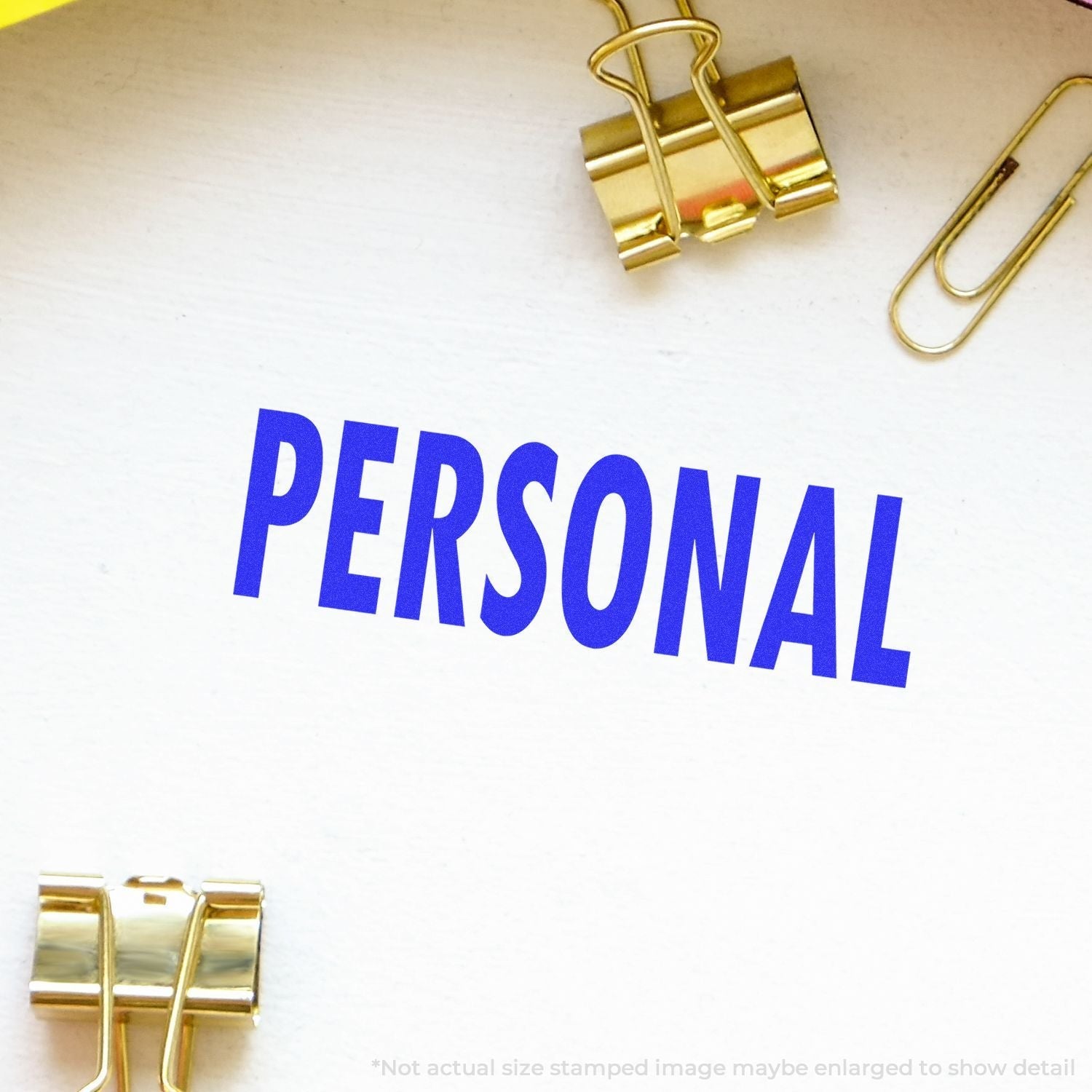 Self Inking Personal Stamp imprinting the word PERSONAL in blue on paper, surrounded by gold binder clips and a paperclip.