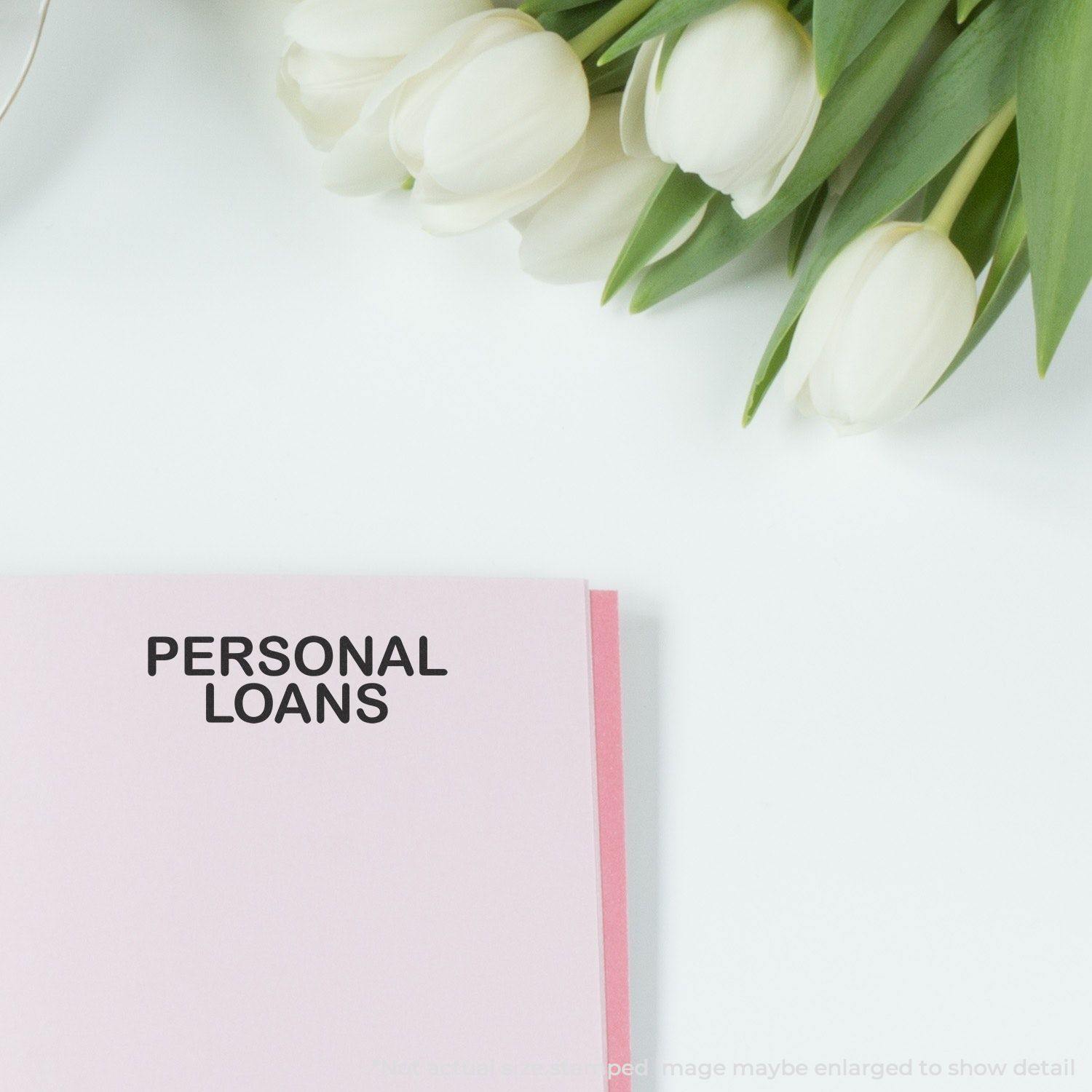 Large Self Inking Personal Loans Stamp used on a pink document, with white tulips in the background on a white surface.