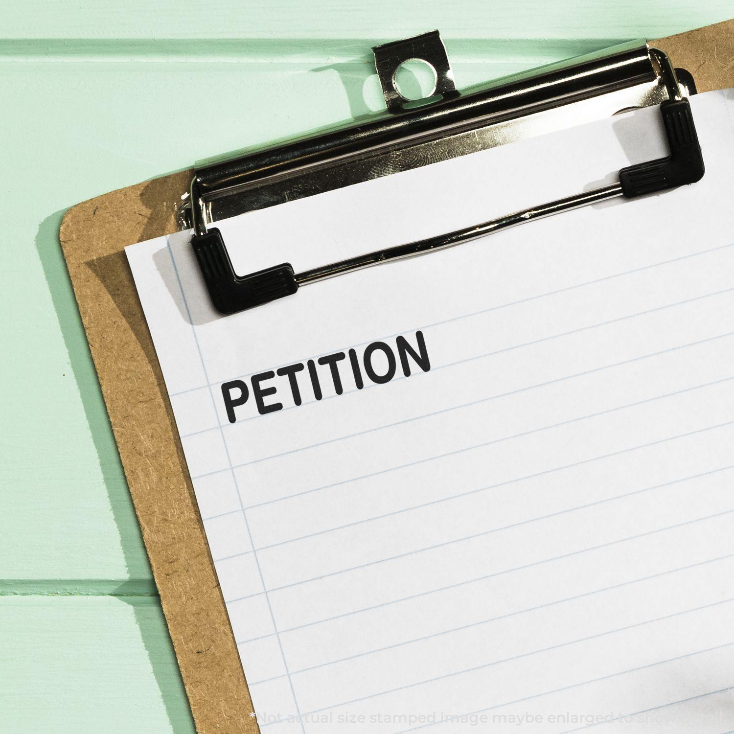 Clipboard with a sheet of paper stamped with the word PETITION using a rubber stamp.