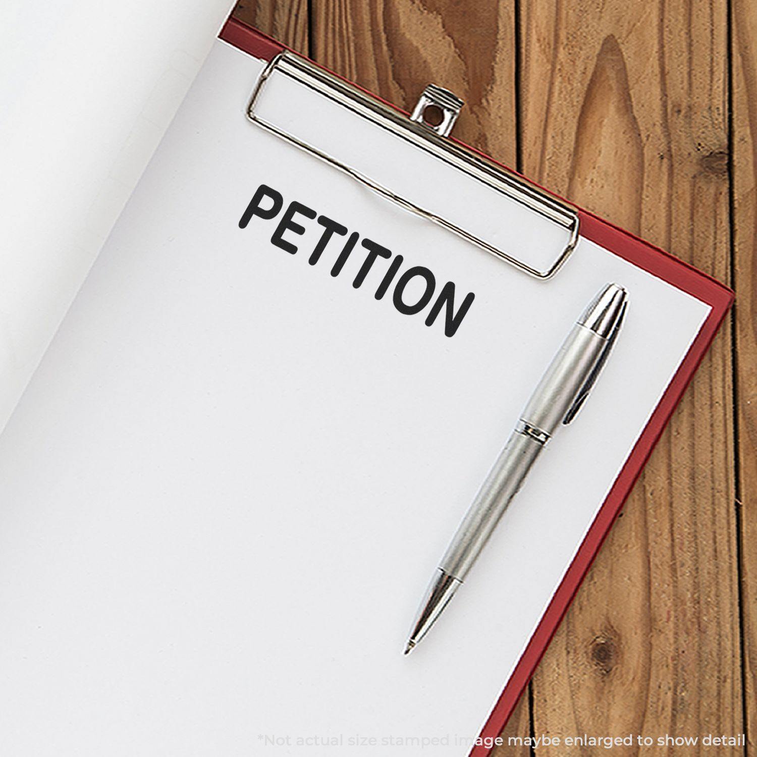 A clipboard with a paper stamped PETITION using the Large Petition Rubber Stamp, accompanied by a silver pen on a wooden surface.