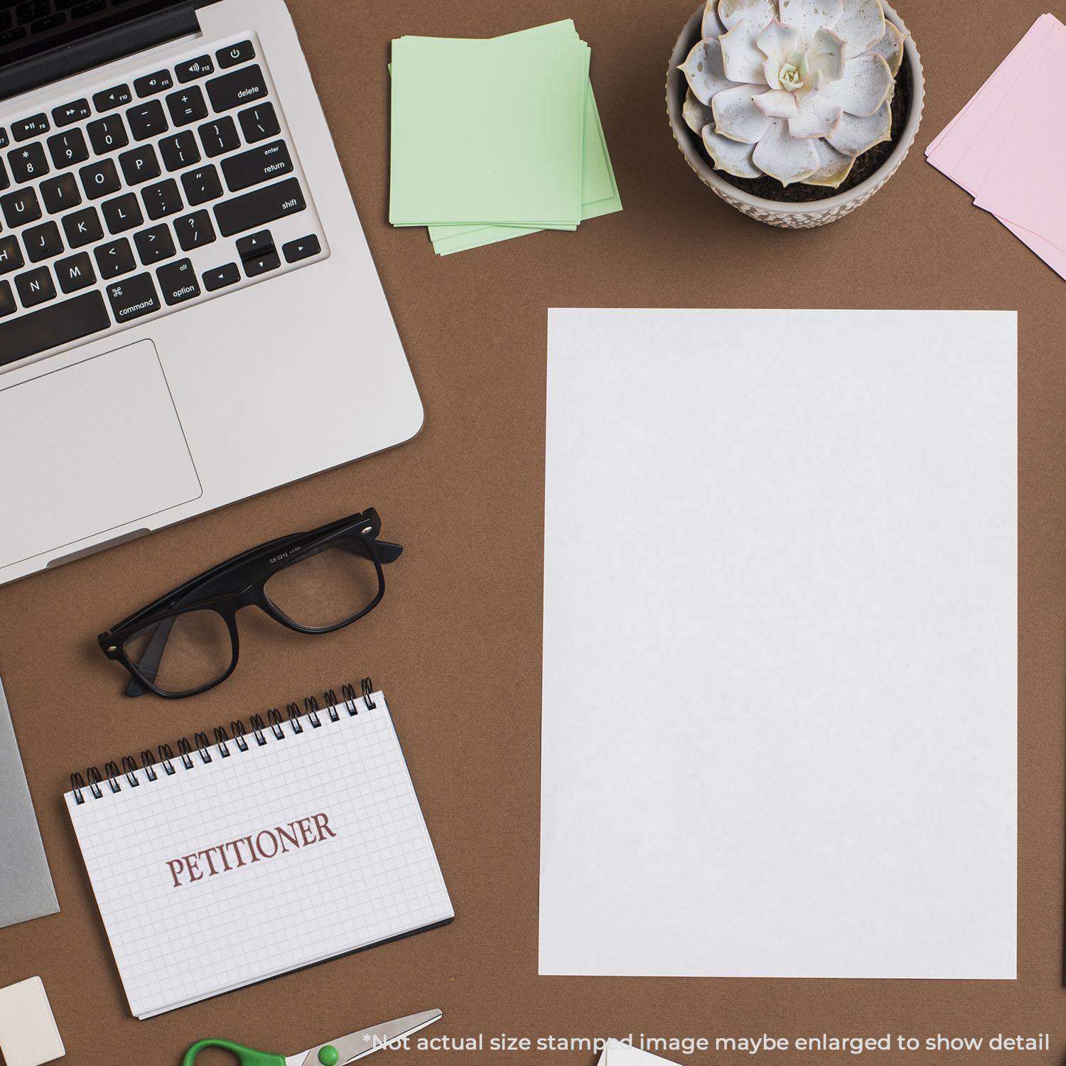 Desk with a Large Petitioner Rubber Stamp, glasses, laptop, notepad, succulent, and blank paper. Text reads PETITIONER on the notepad.