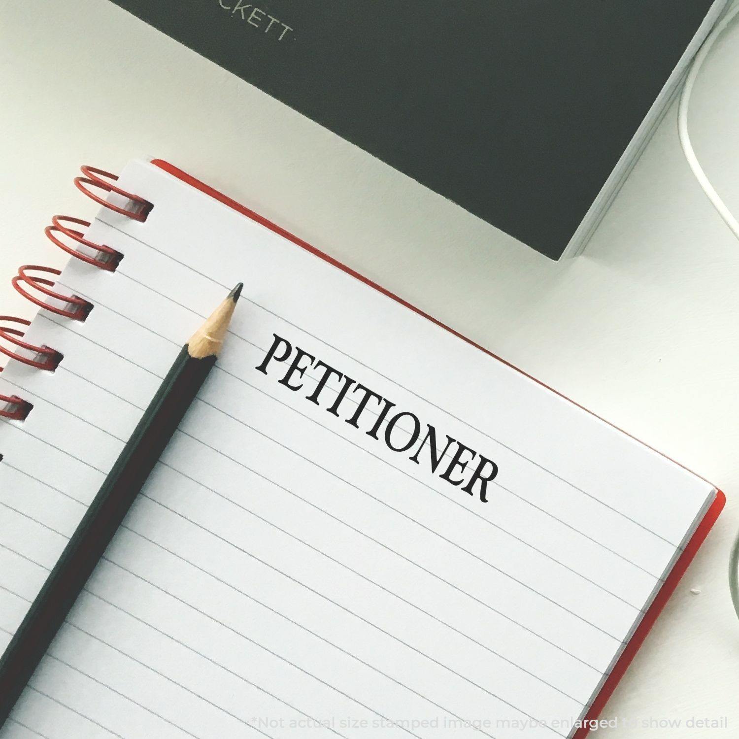 Large Petitioner Rubber Stamp used on a lined notebook page with a pencil beside it.