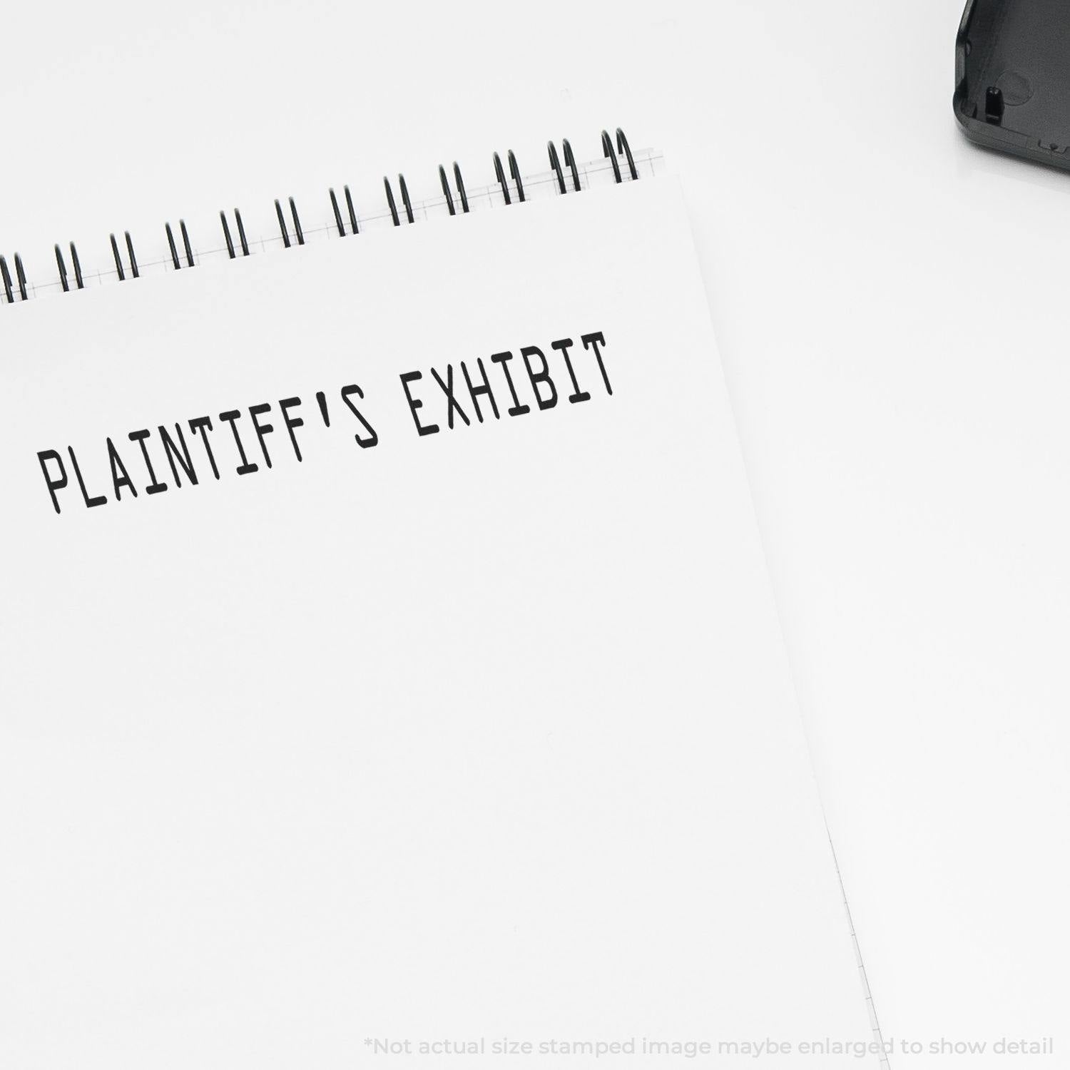 Large Plaintiffs Exhibit Rubber Stamp imprint on a white notepad, with a black ink pad partially visible in the top right corner.